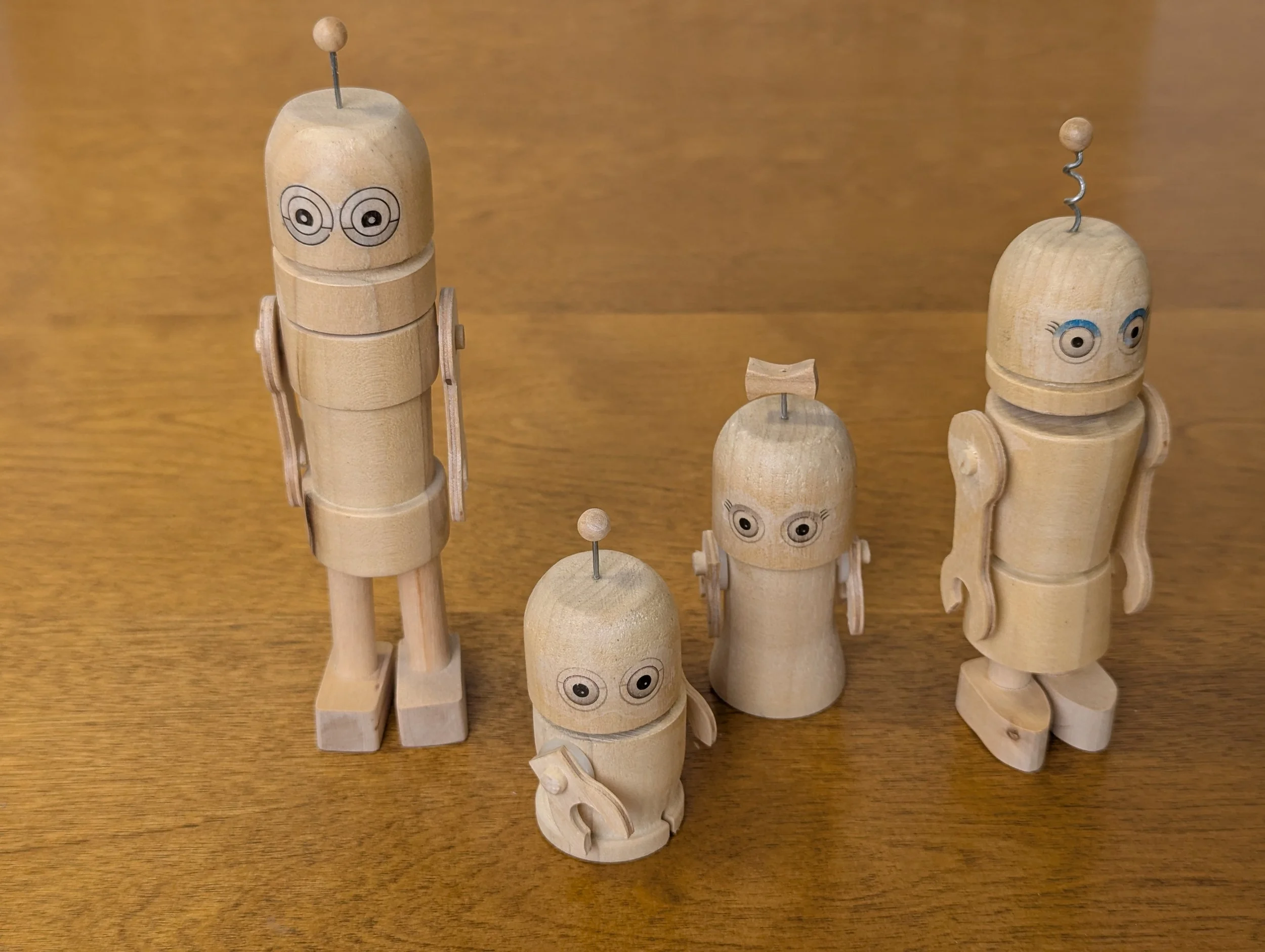 Collection of wooden robot figurines with painted eyes on a wooden surface.