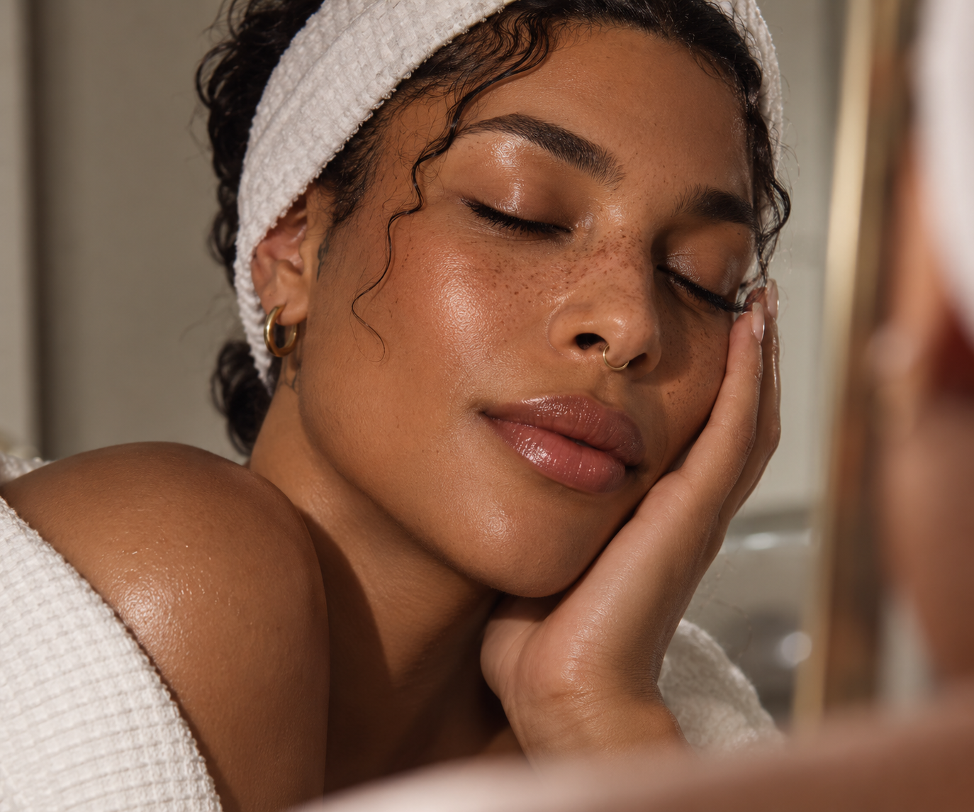 Close-up portrait of a gender-expansive person with warm brown skin, freckles and glowing skin.