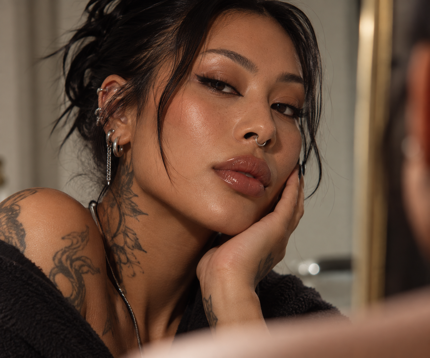 Close-up portrait of a feminine-presenting person with tattoos, piercings and glowing skin.