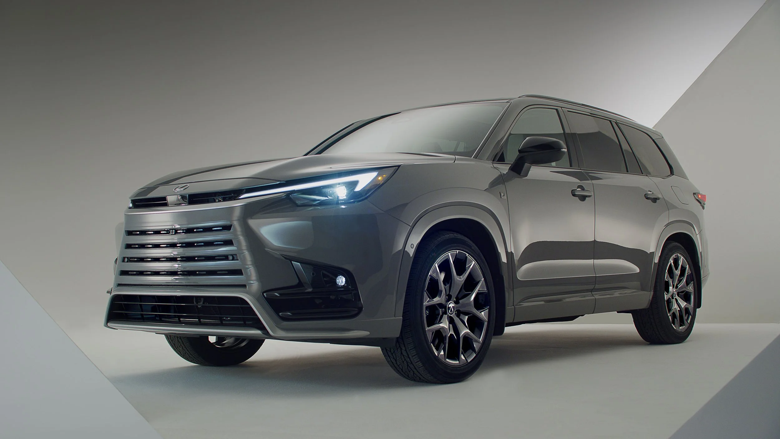 A gray SUV with modern design features, including sleek headlights and a prominent front grille, parked indoors against a plain background.