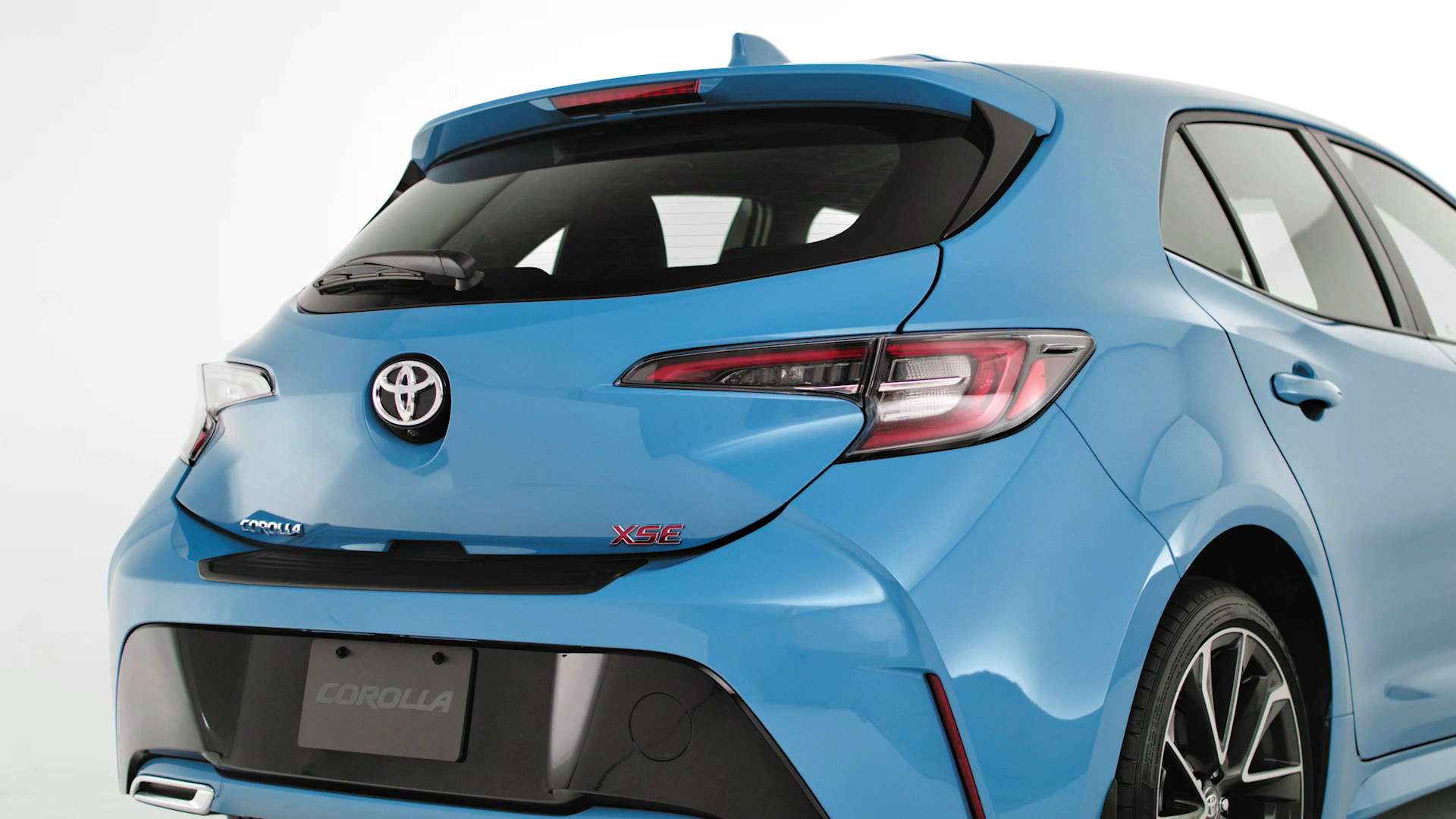 Rear view of a blue Toyota Corolla hatchback with 'XSE' badge, distinctive taillights, rear windshield, and part of the right side door visible.
