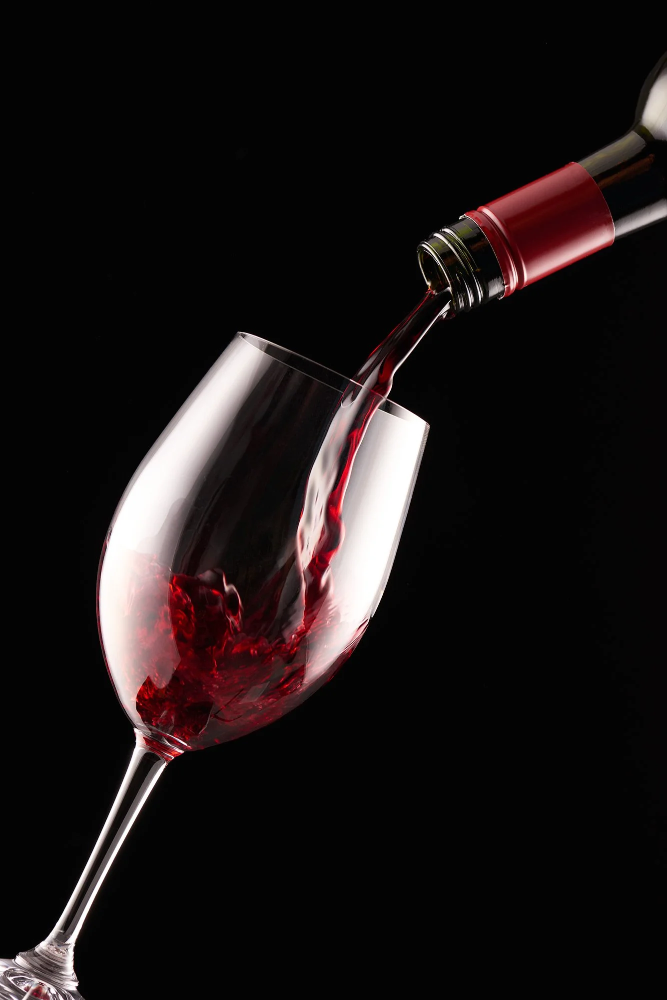 Red wine being poured into a wine glass against a black background.