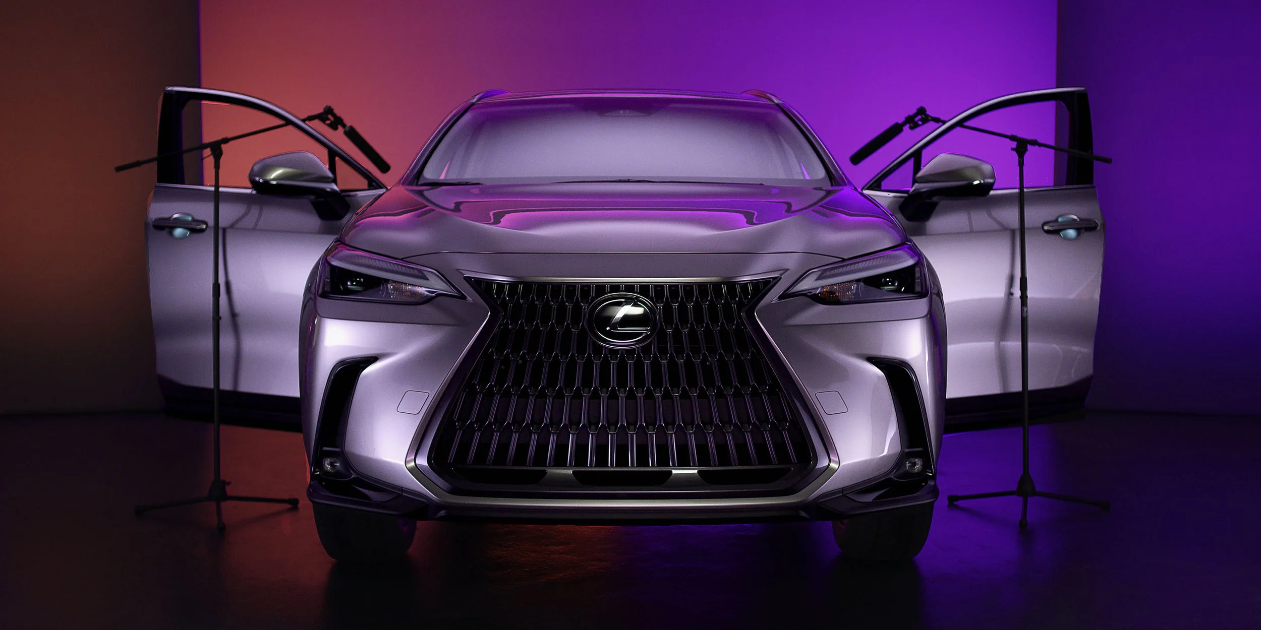 A silver Lexus car in a studio with purple and pink lighting, with open front and rear doors.
