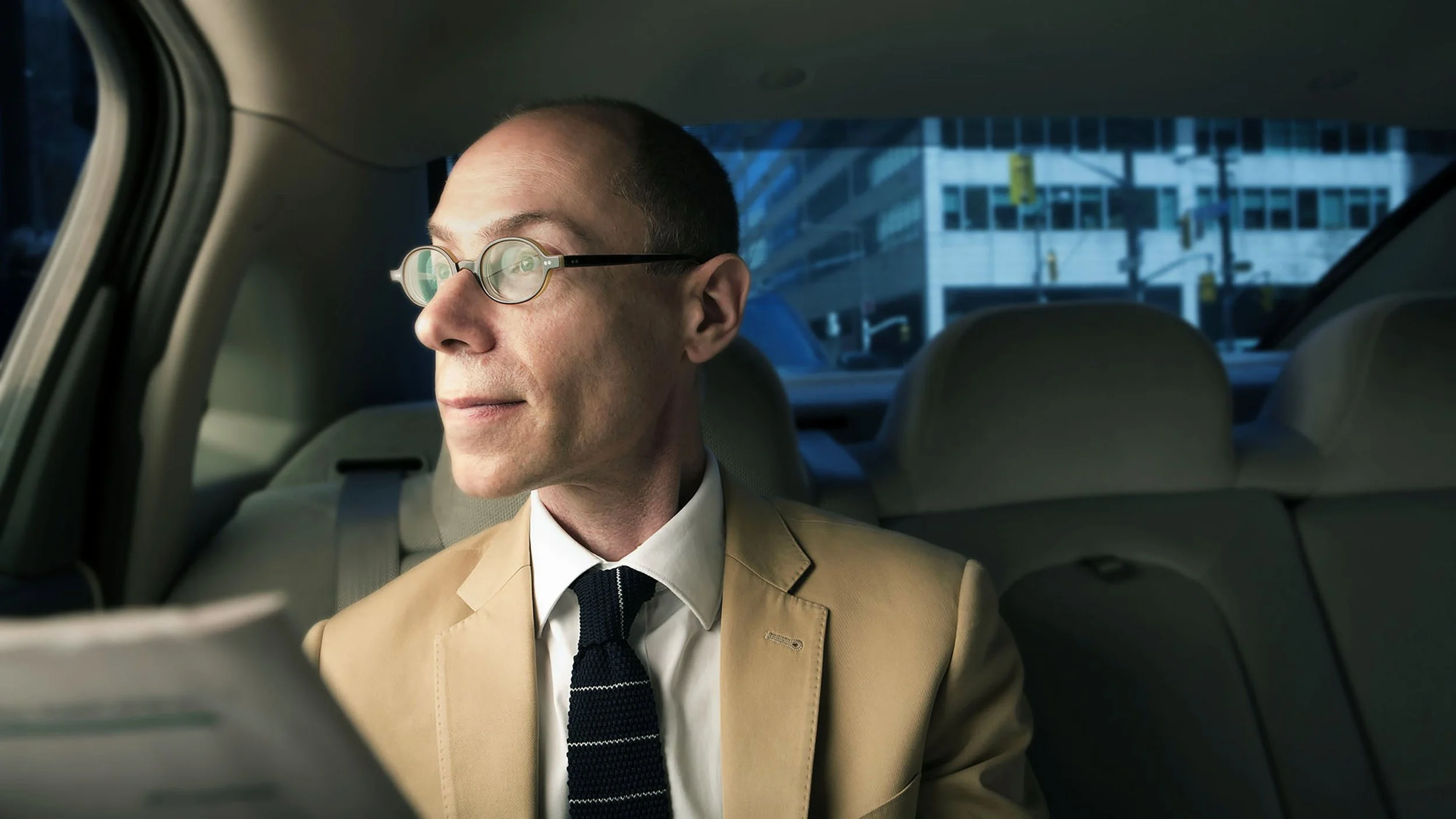 Environmental corporate portrait of a man in a suit seated in the back of a car, photographed in the city