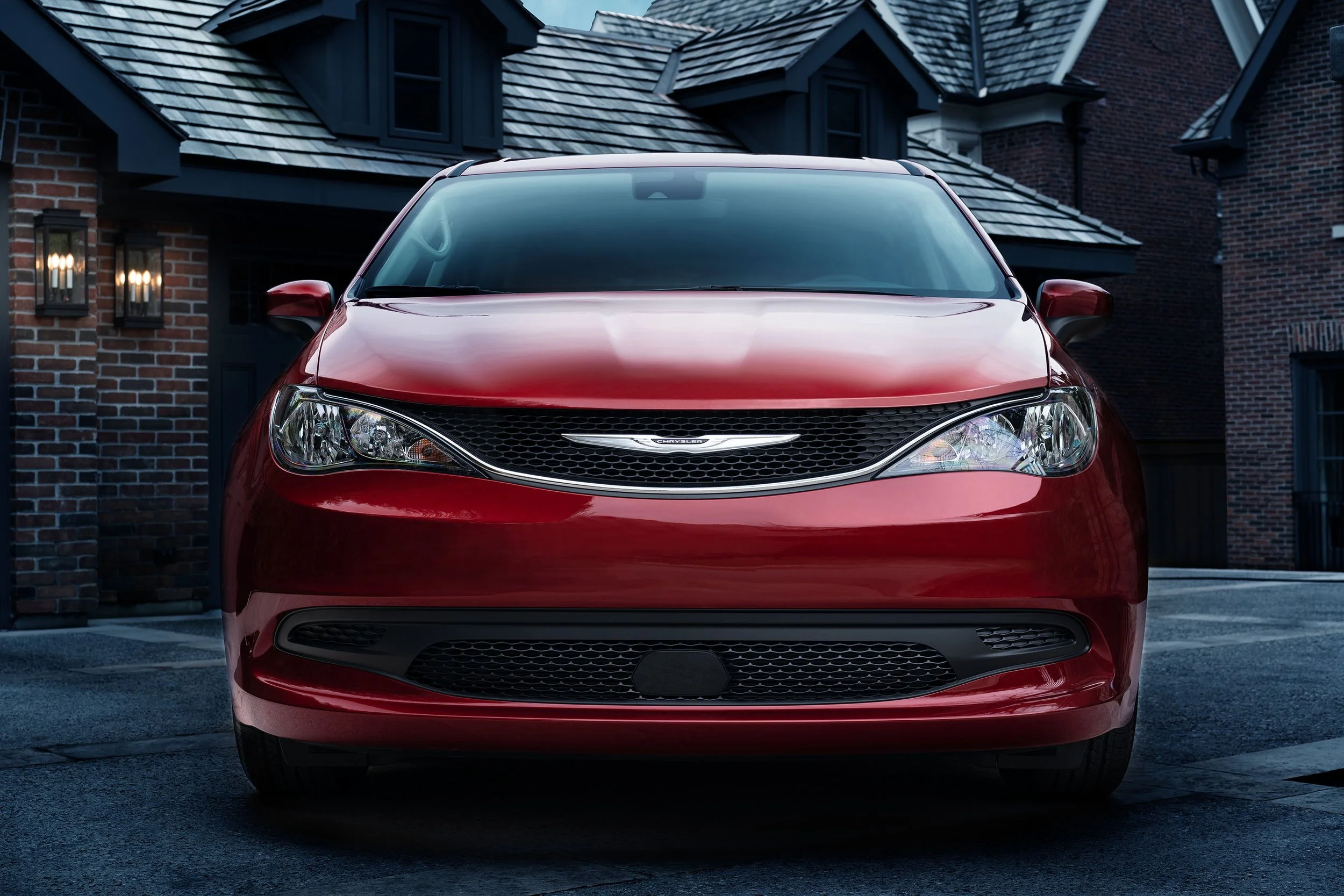 Front view of a red Chrysler SUV parked in front of a house with brick and dark-colored siding, and a shingled roof.