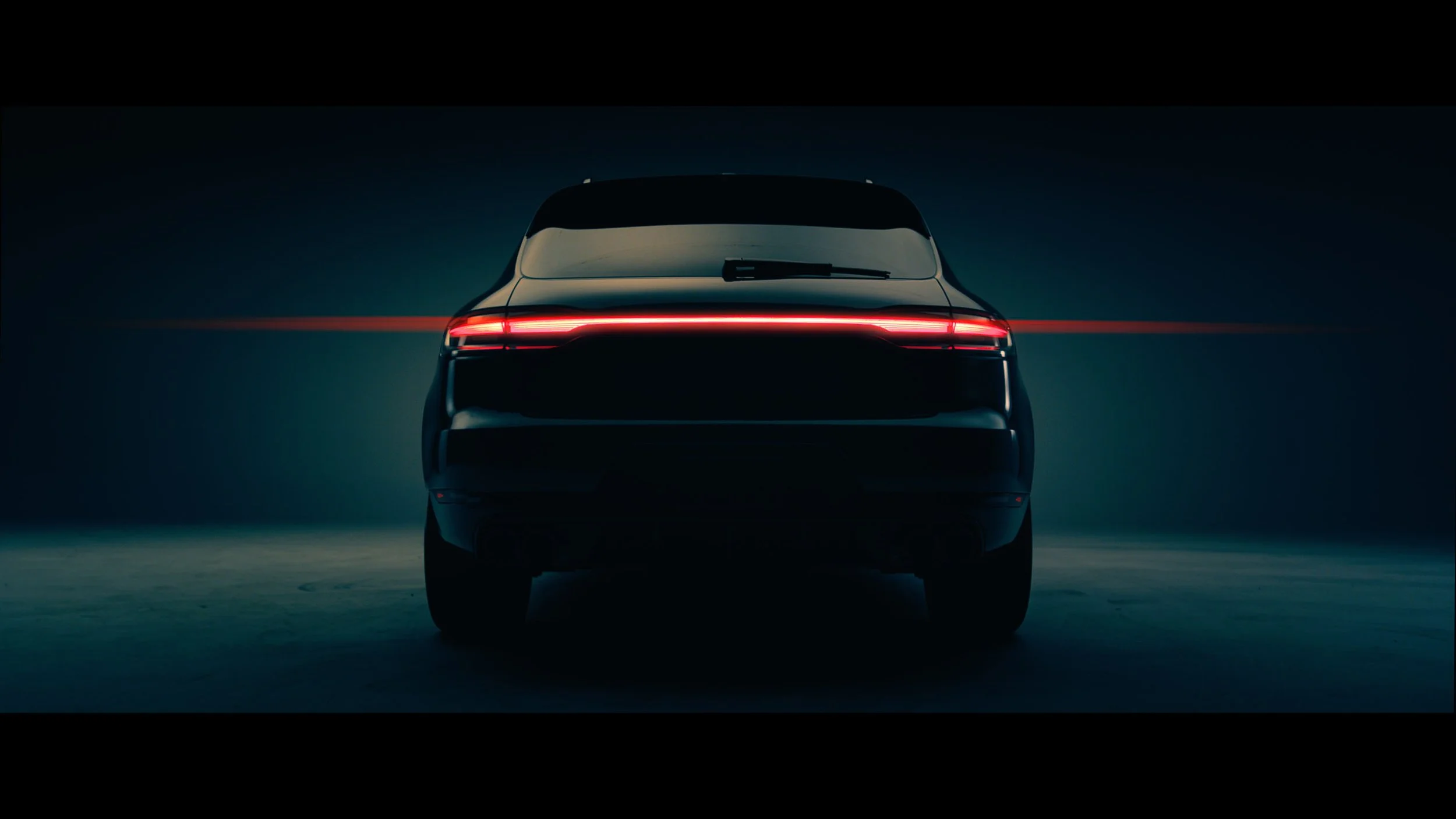 Rear view of a car with a continuous horizontal red LED taillight in a dark, minimalist setting.