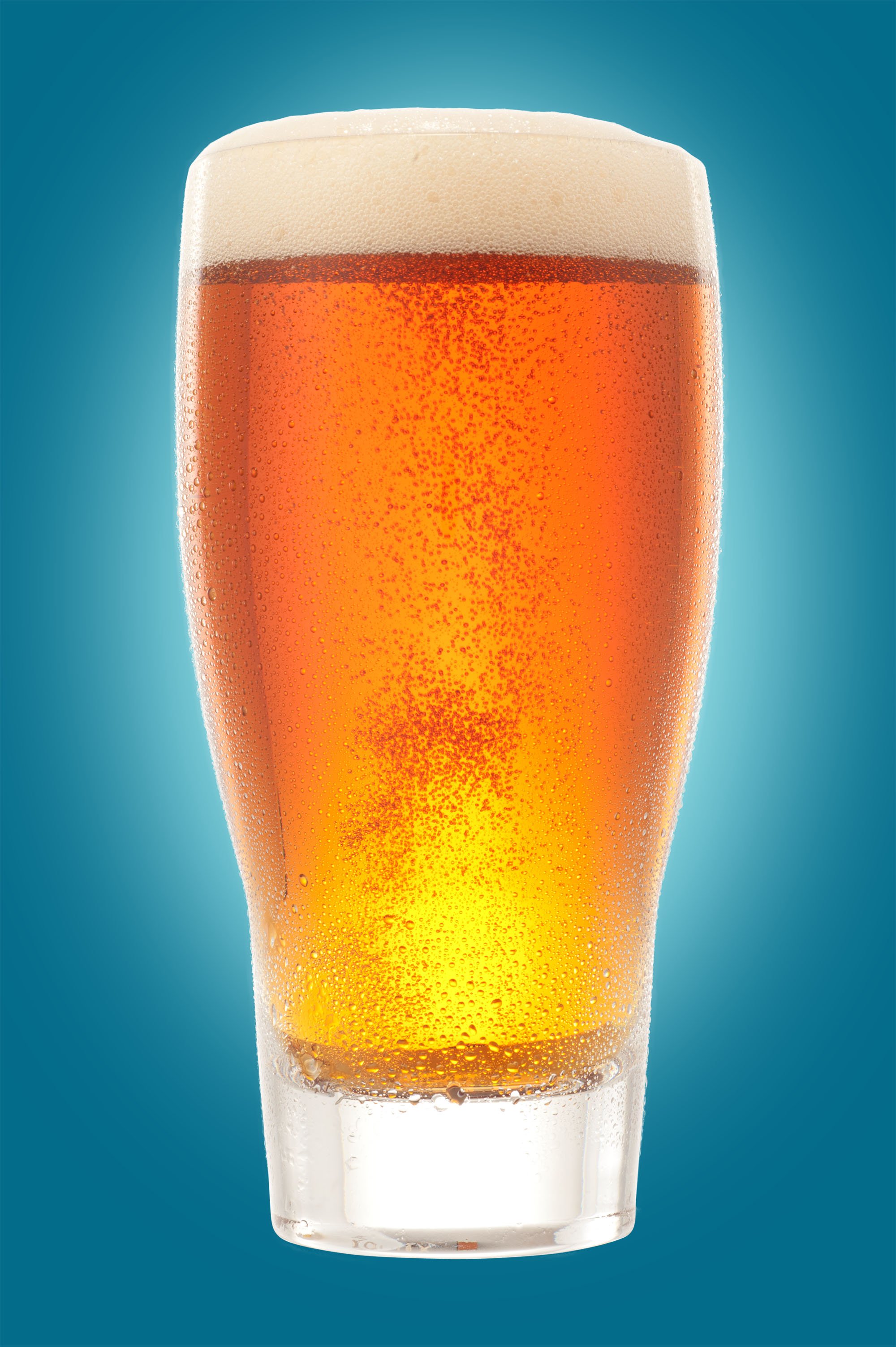 Close-up of a glass of amber-colored beer with a frothy white head, condensation on the outside, against a blue background.