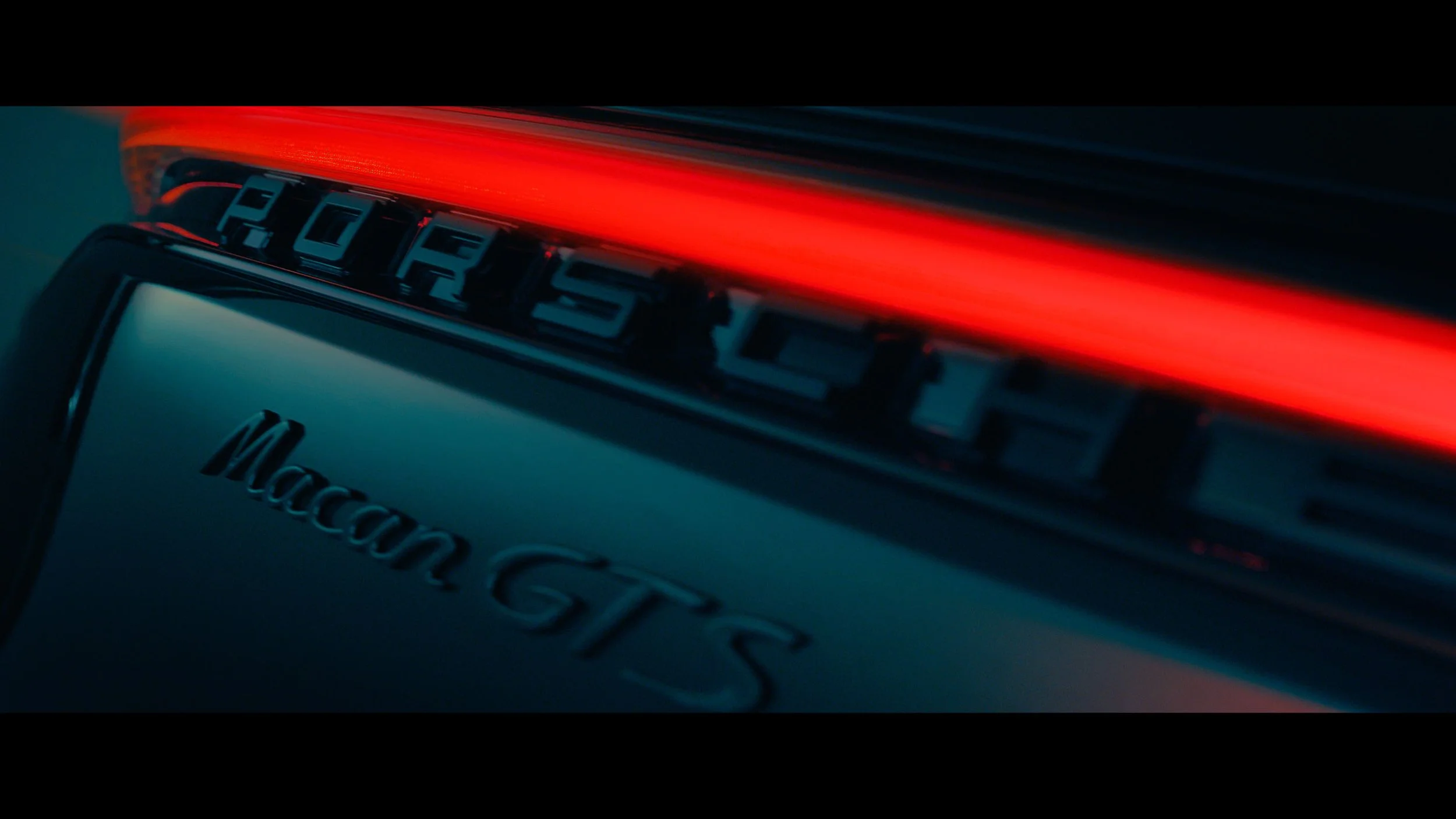 Close-up of the rear of a black Porsche Macan S with red taillights on at night.