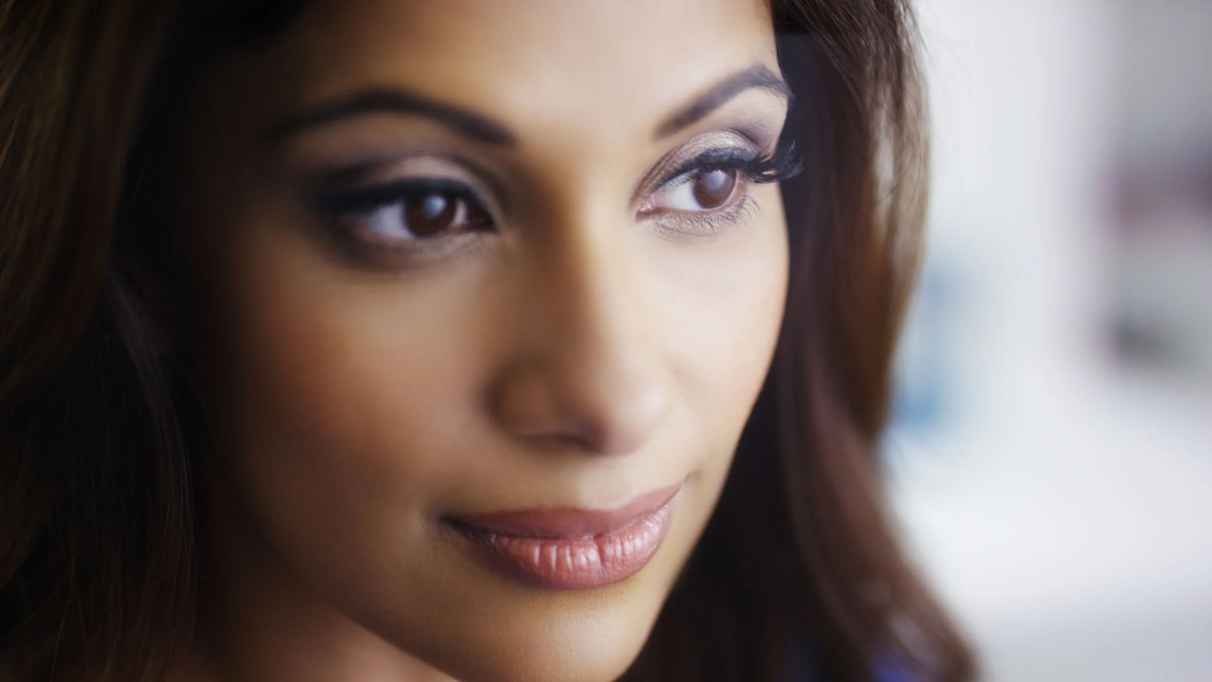 Close-up of a woman's face with makeup, focusing on her eyes and lips, brown hair, and smooth skin.