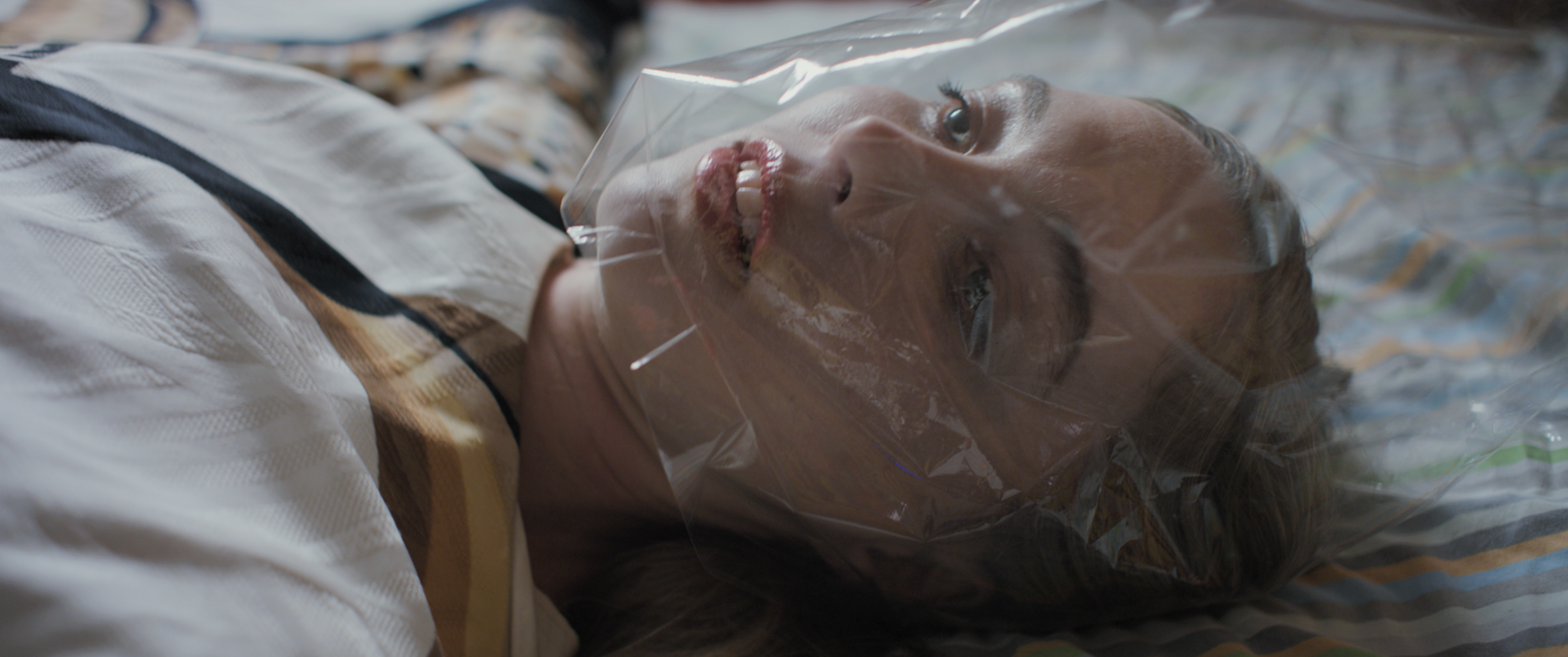 A woman lying on a bed with a plastic oxygen mask over her face, appearing to be unconscious or asleep.