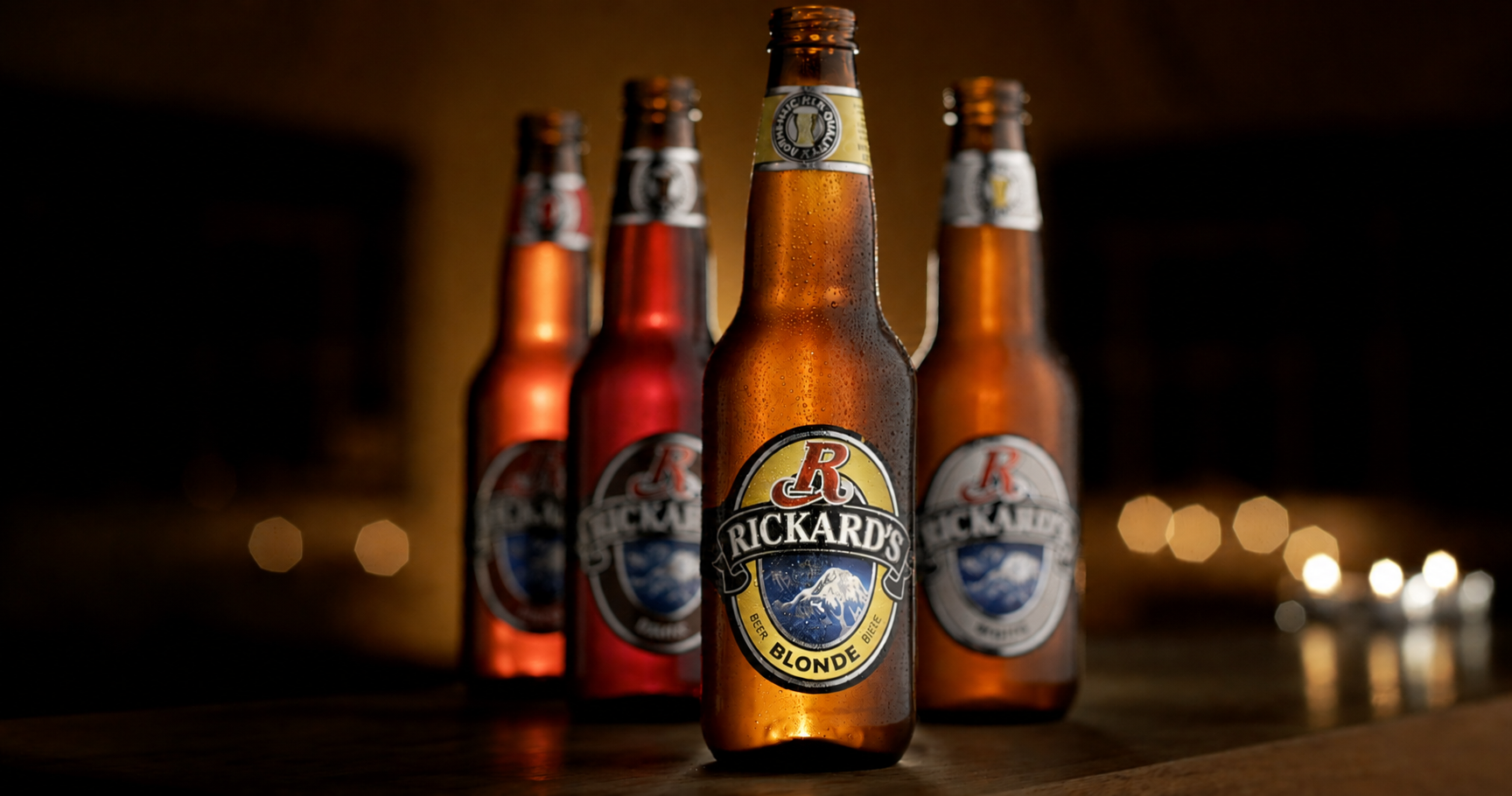 Four bottles of Rickard’s Blonde beer arranged on a wooden surface.