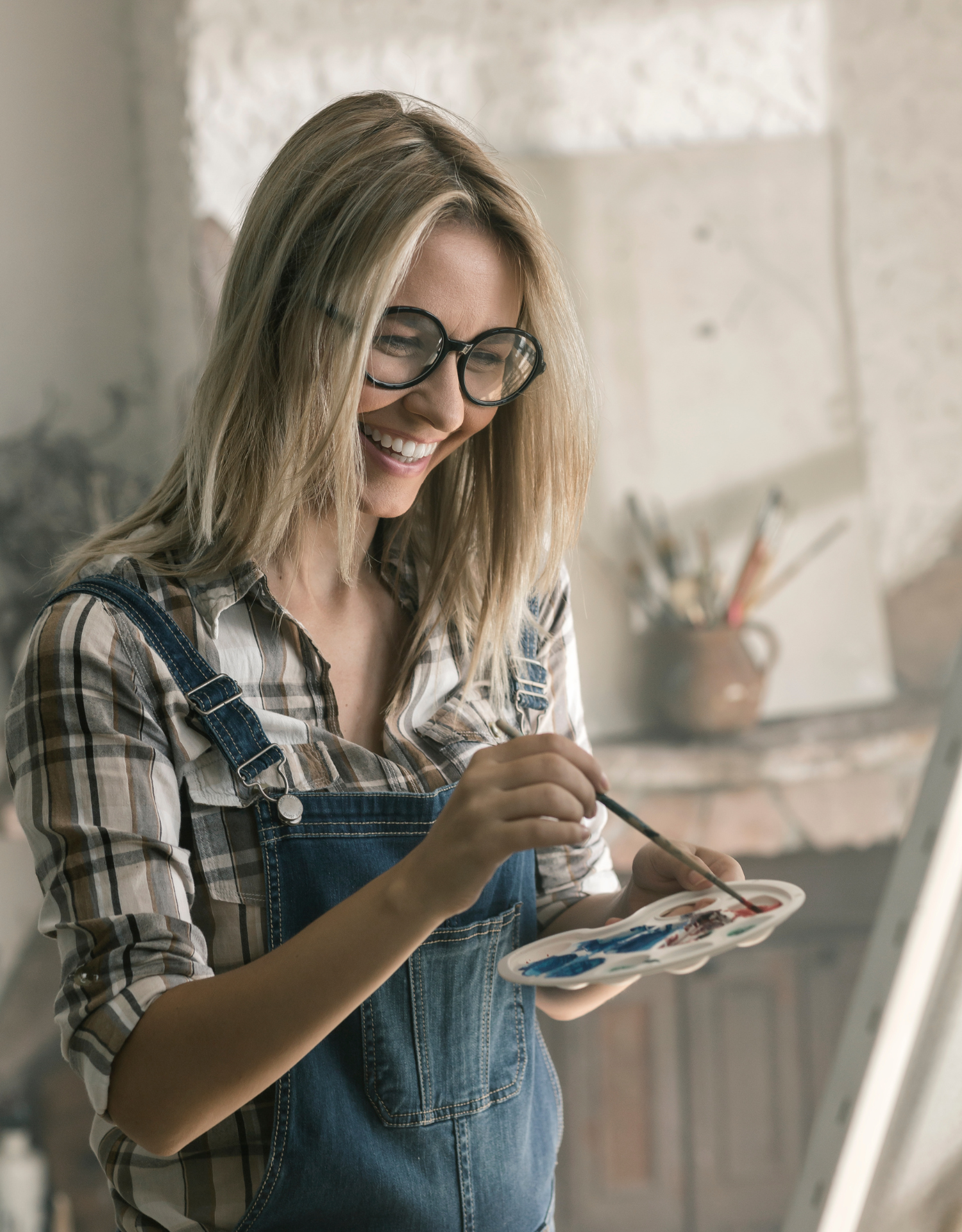 Woman with blonde hair and glasses painting on a canvas in an art studio