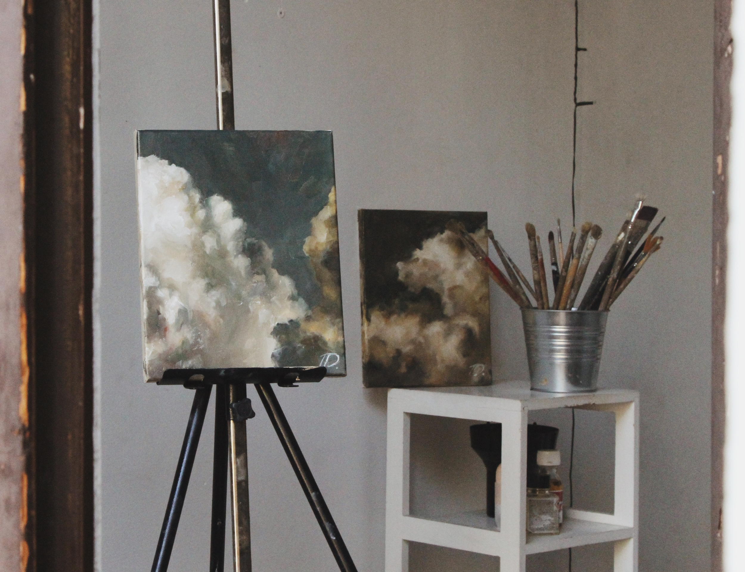 An art studio with paintings and brushes on display, seen through a doorway.