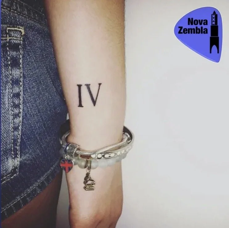 Tattoo van het Romeinse getal IV op de onderarm, met armbanden en een bedel met de Britse vlag.