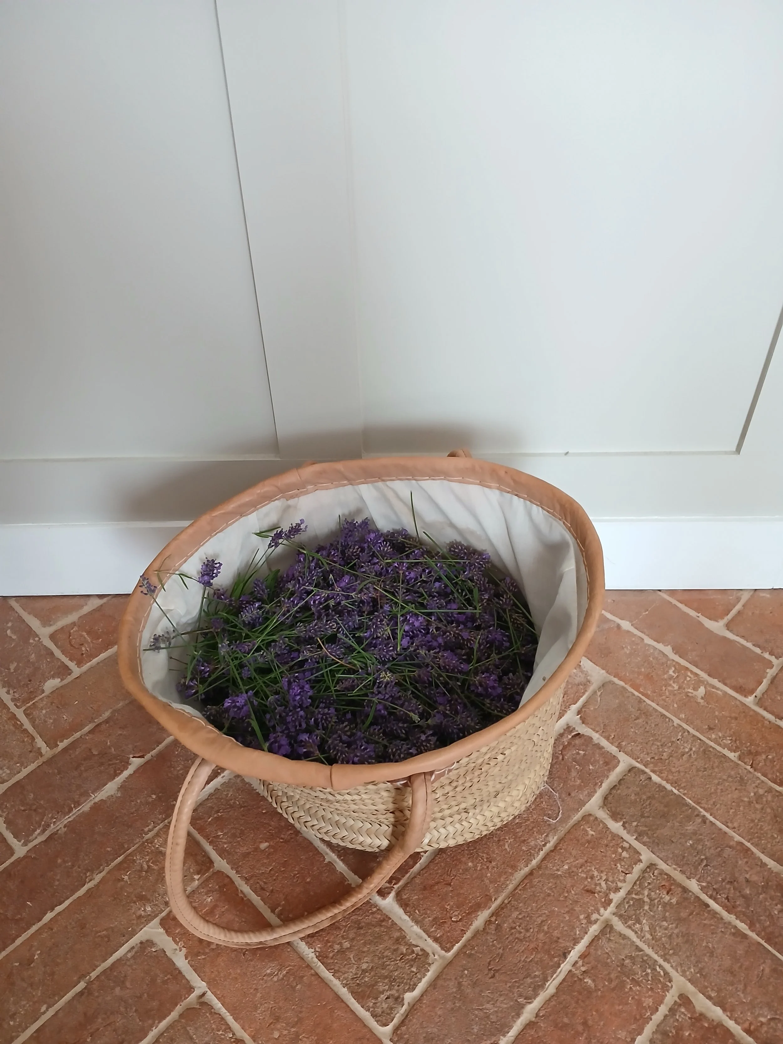 A basket filled with purple lavender flowers sitting on a tiled floor next to a white wall or cabinet.