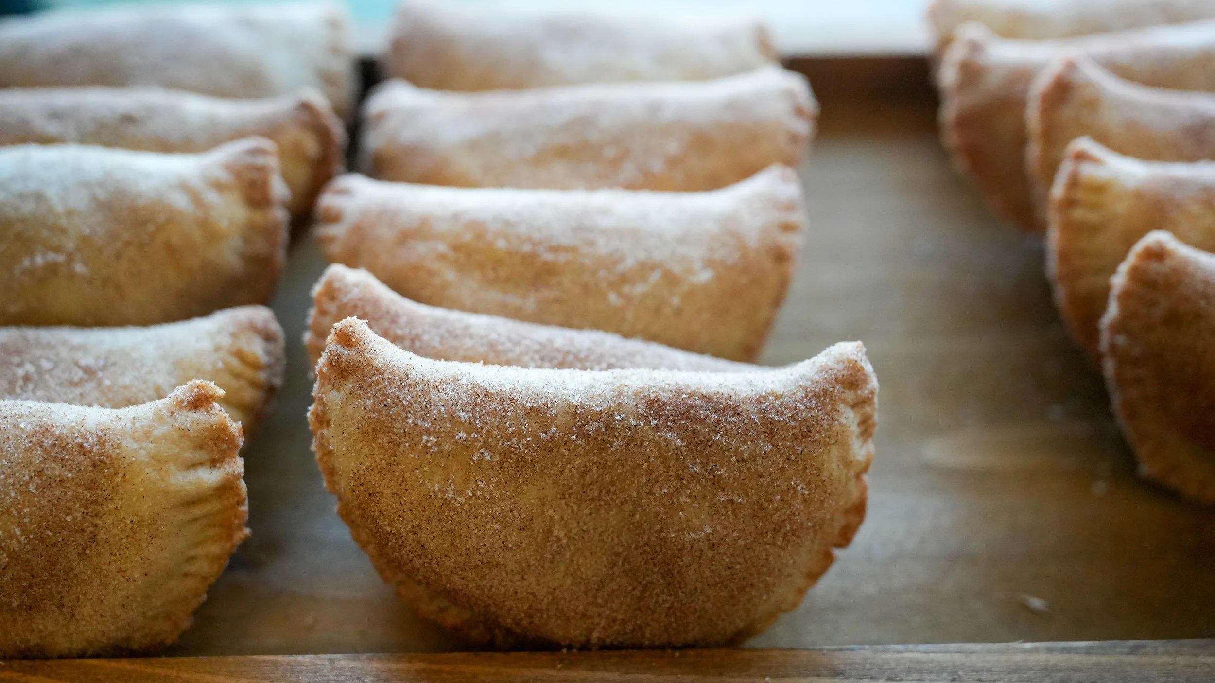 Close-up of baked empanadas sprinkled with sugar on a baking sheet.