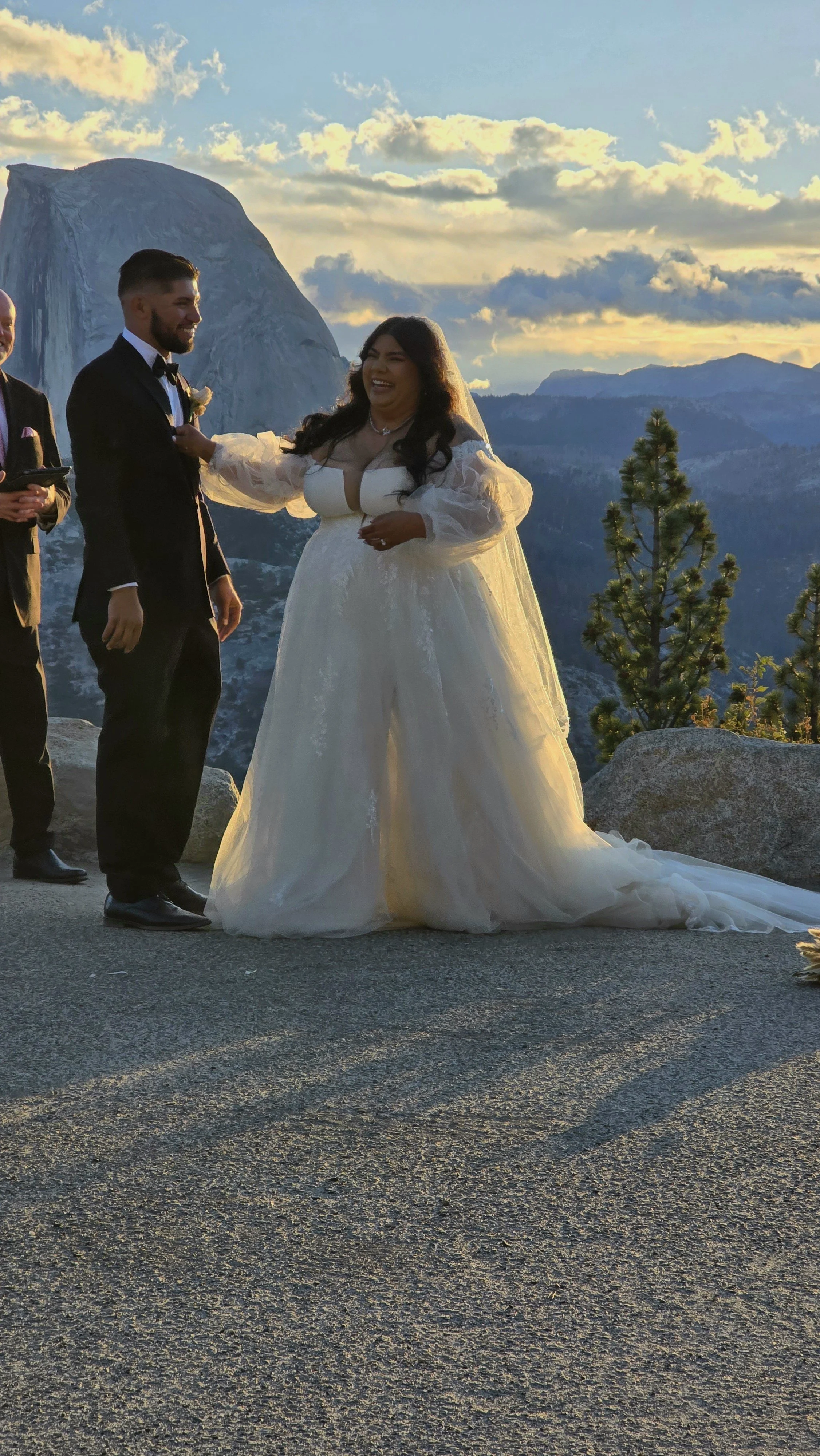 Bride and groom exchanging vows at outdoor wedding with mountain and forest background during sunset.