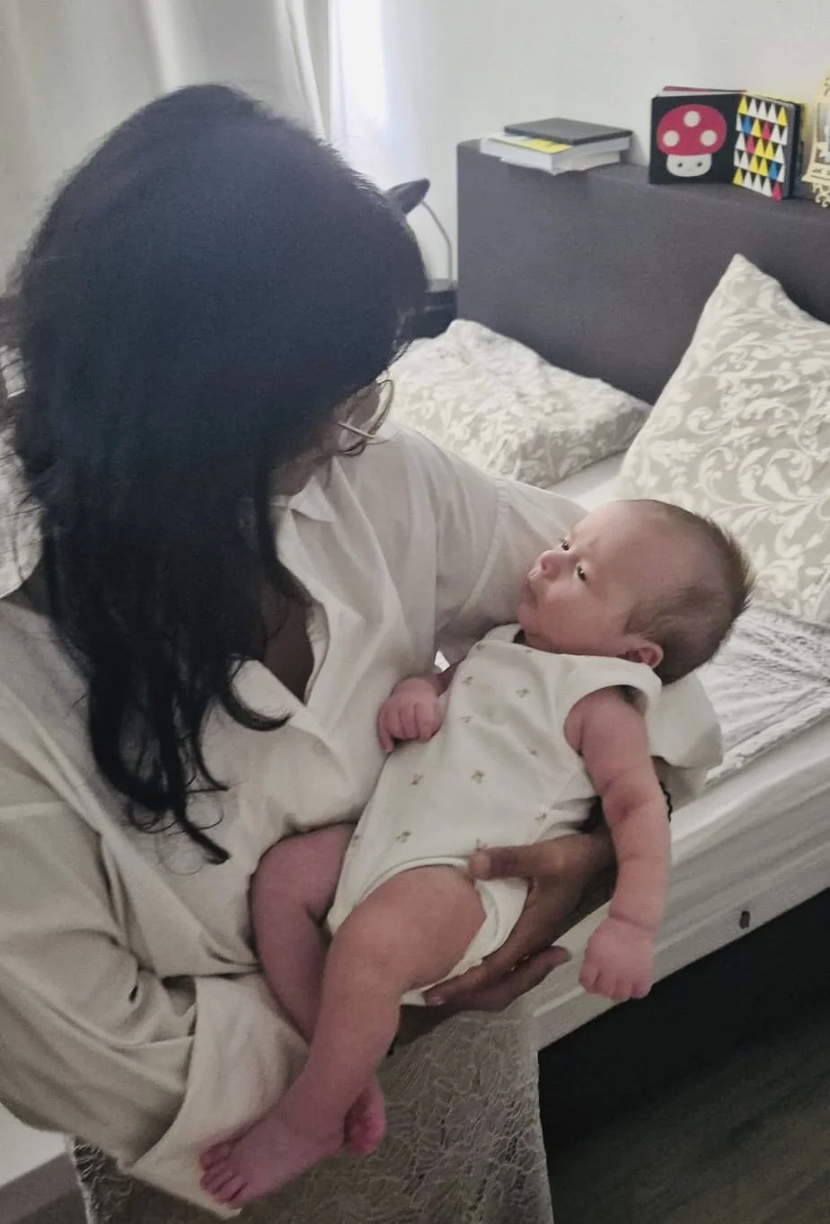 Een vrouw houdt een baby in haar armen terwijl ze op een bed zit.