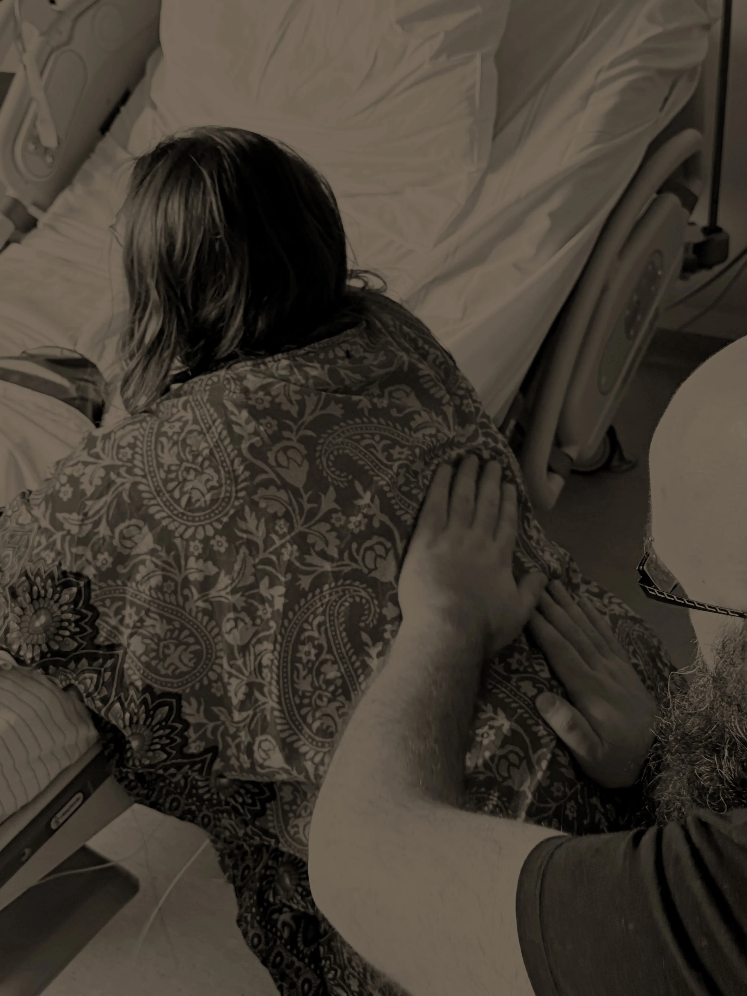 Persoon ligt in ziekenhuisbed, bed wordt verzorgd door andere persoon, ziekenhuisomgeving.