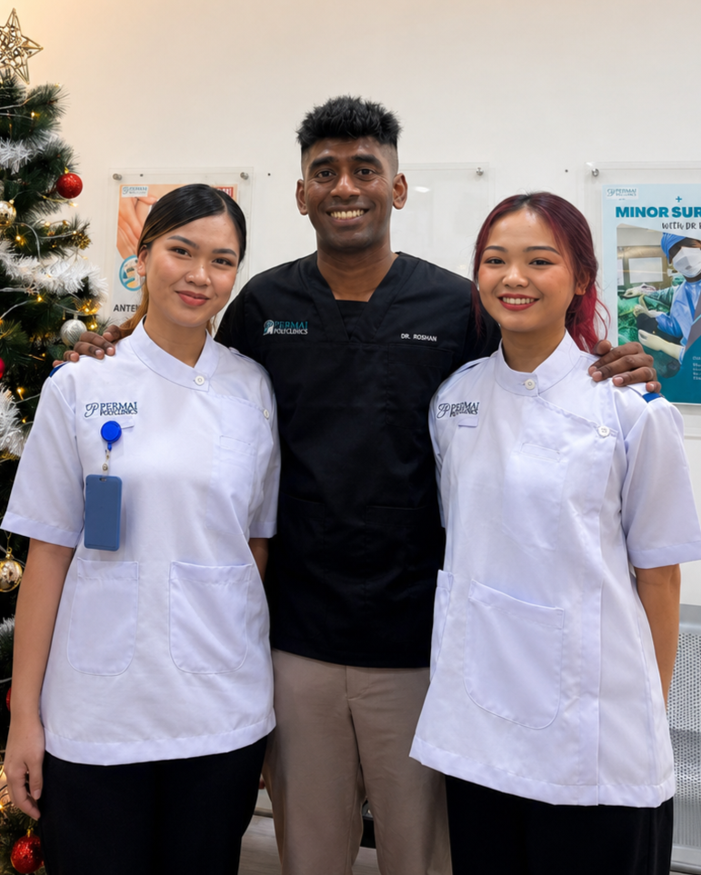 Three healthcare professionals, two female nurses and one male doctor, standing together indoors, smiling, with a decorated Christmas tree on the left and medical posters in the background.