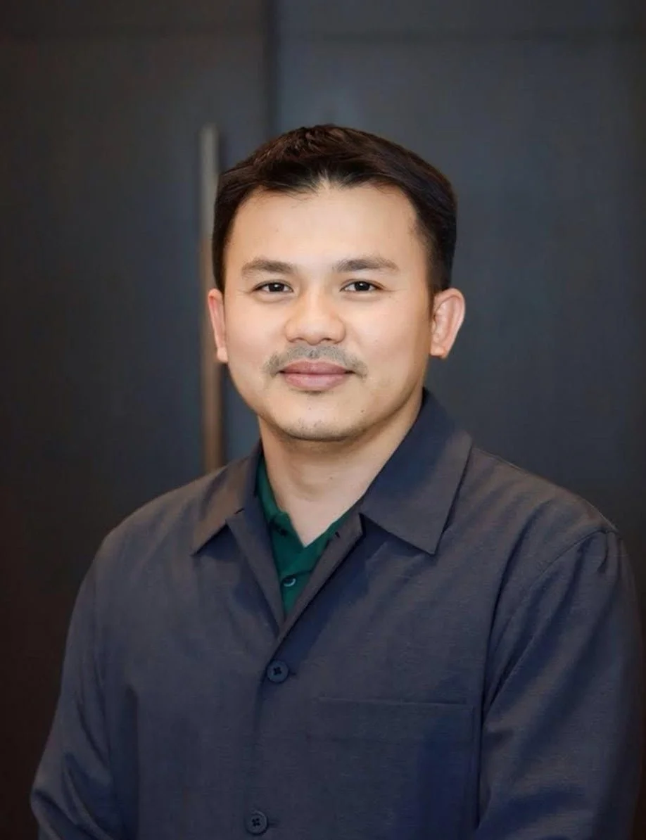 Portrait of a man with short dark hair, light stubble, wearing a dark button-up shirt and a green undershirt, standing against a dark background.
Dr. Saiful Bahri, COO of Permai Polyclinics Group