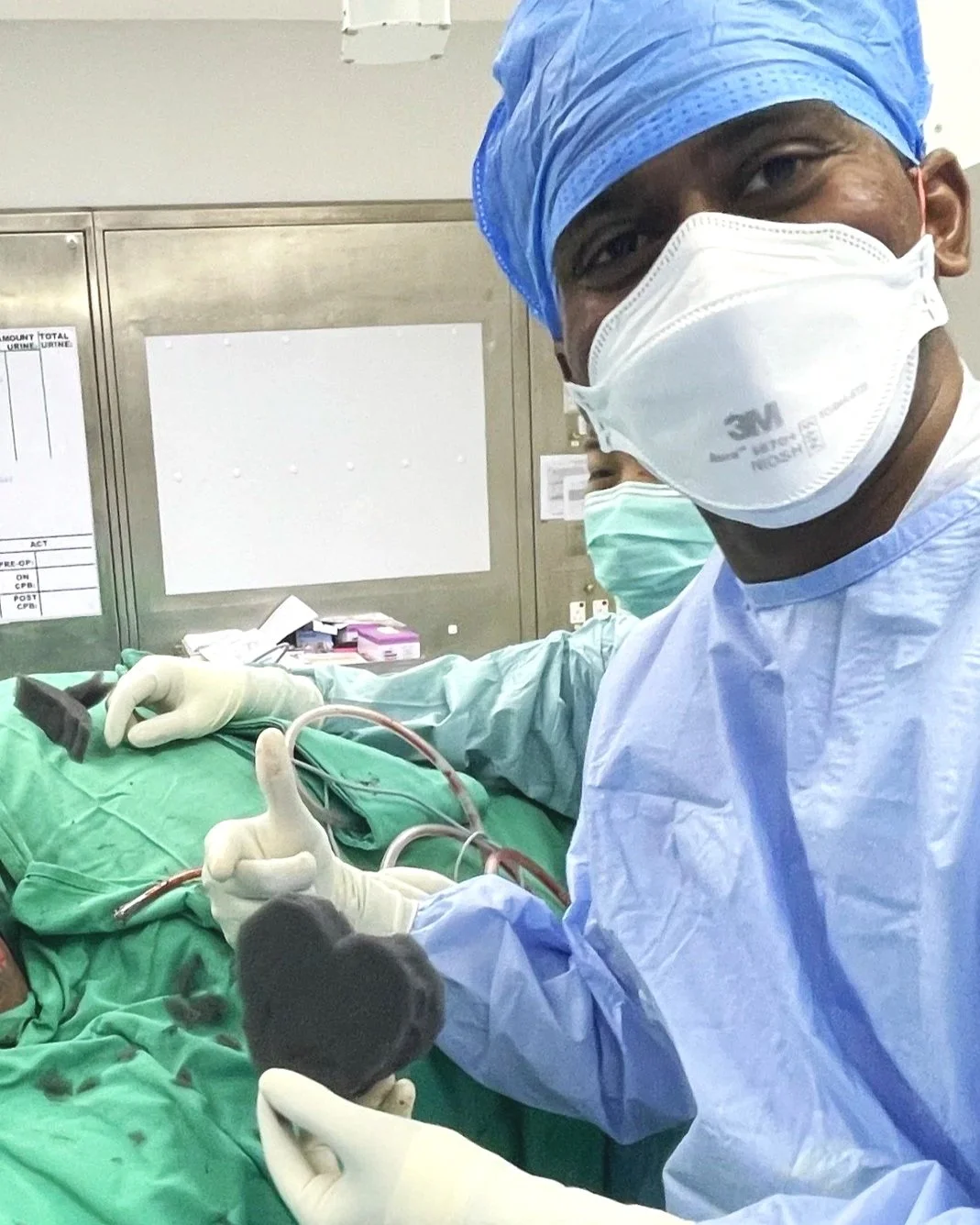 A healthcare worker in surgical scrubs and mask giving a thumbs up, performing a medical procedure in an operating room.