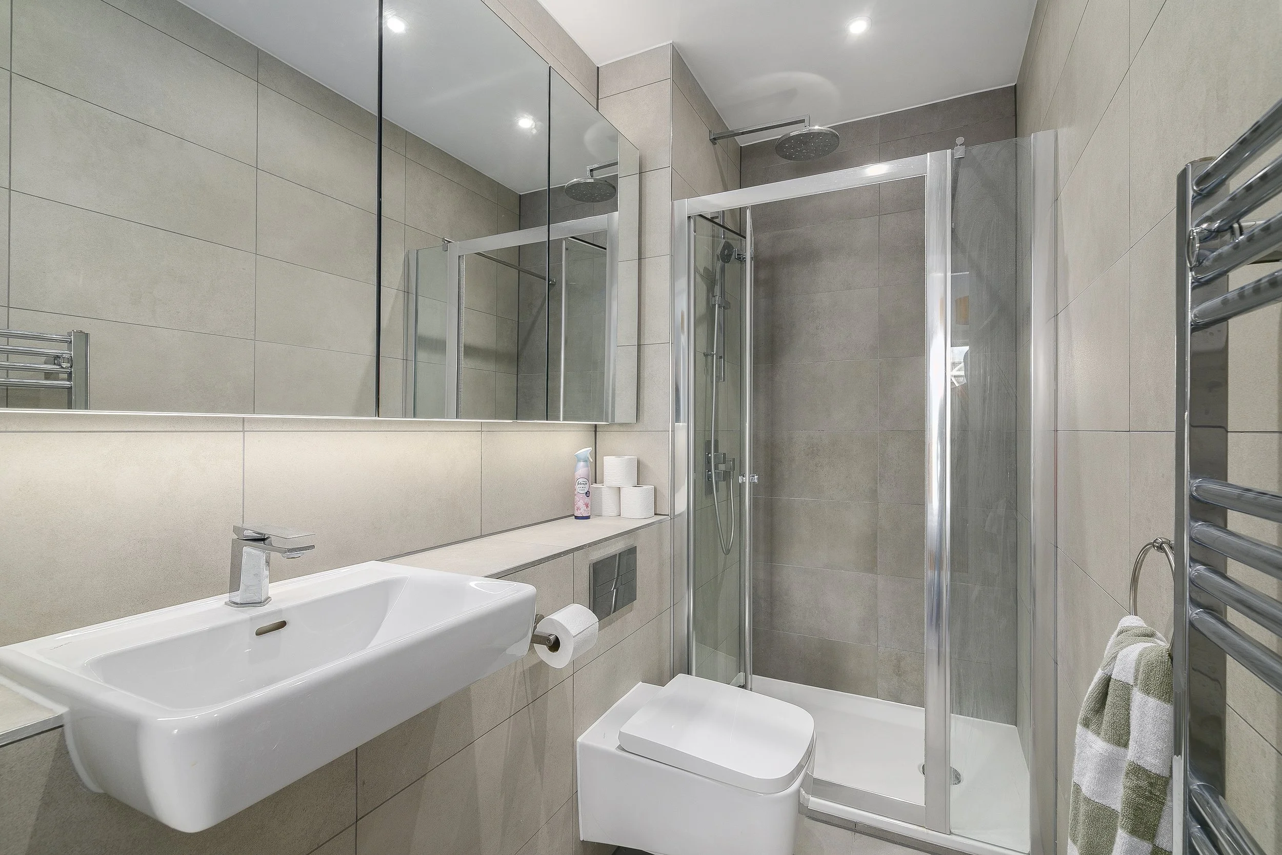 Modern bathroom with a shower enclosure, wall-mounted sink, and mirror, featuring beige tiles and chrome fixtures.