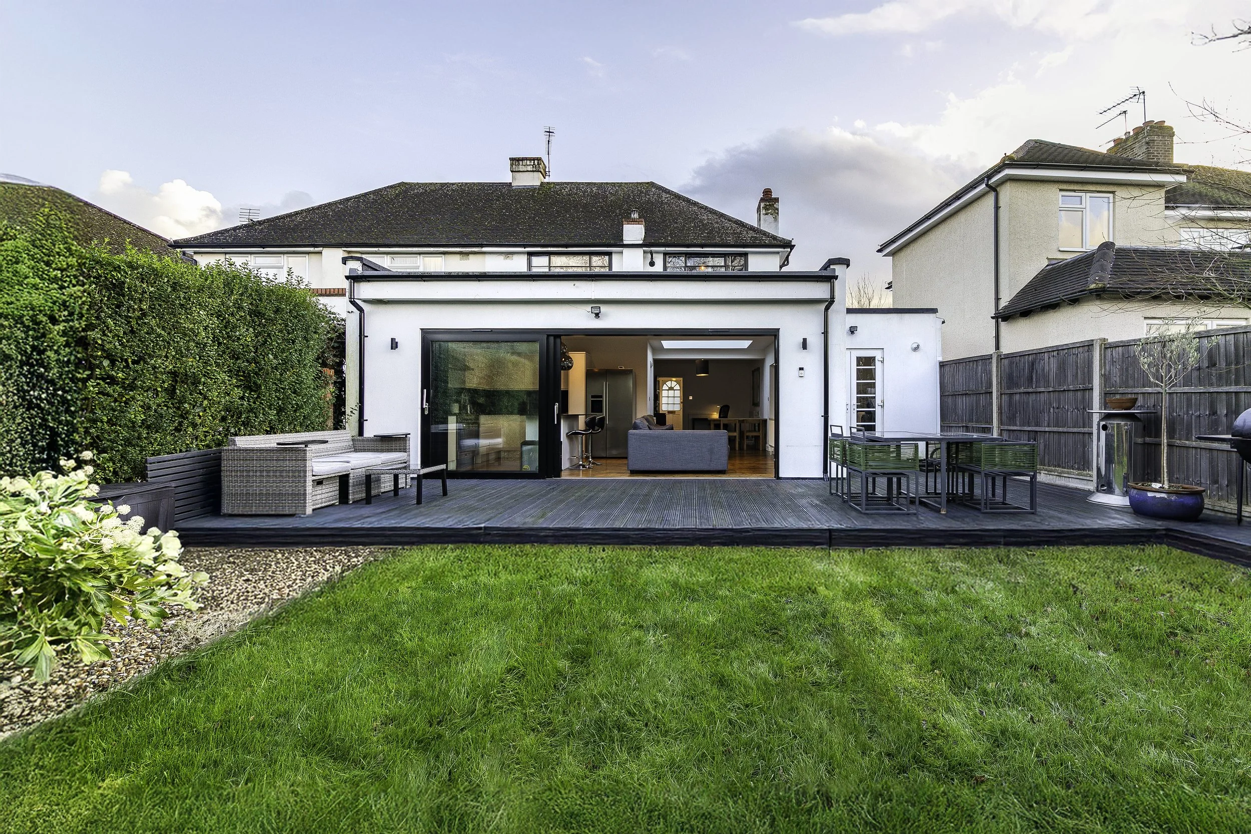 Backyard with a modern patio, outdoor furniture, and a view of neighboring houses under a cloudy sky.