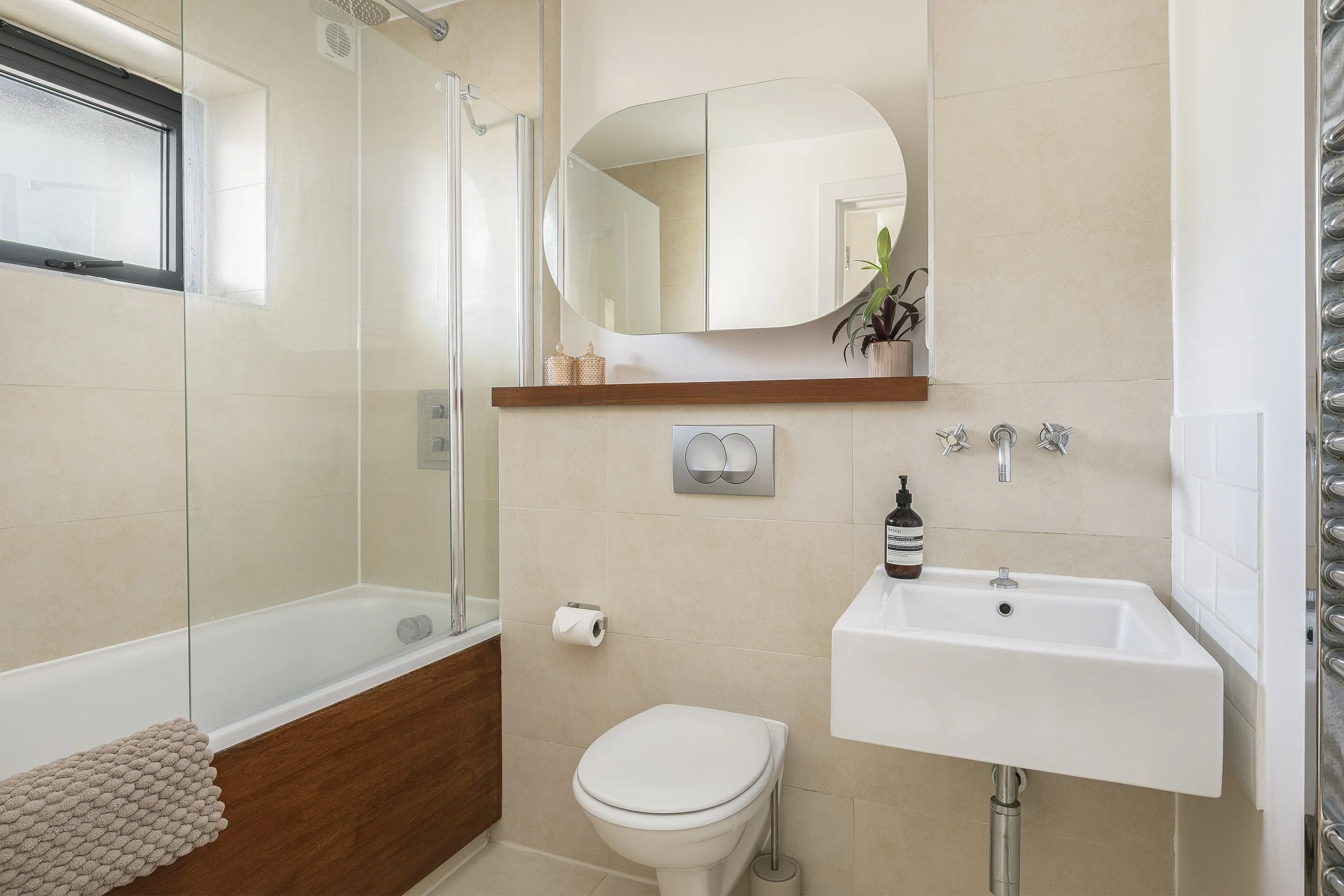 A bathroom with a shower, a mirror, a plant, a toilet, a sink, and a soap dispenser.