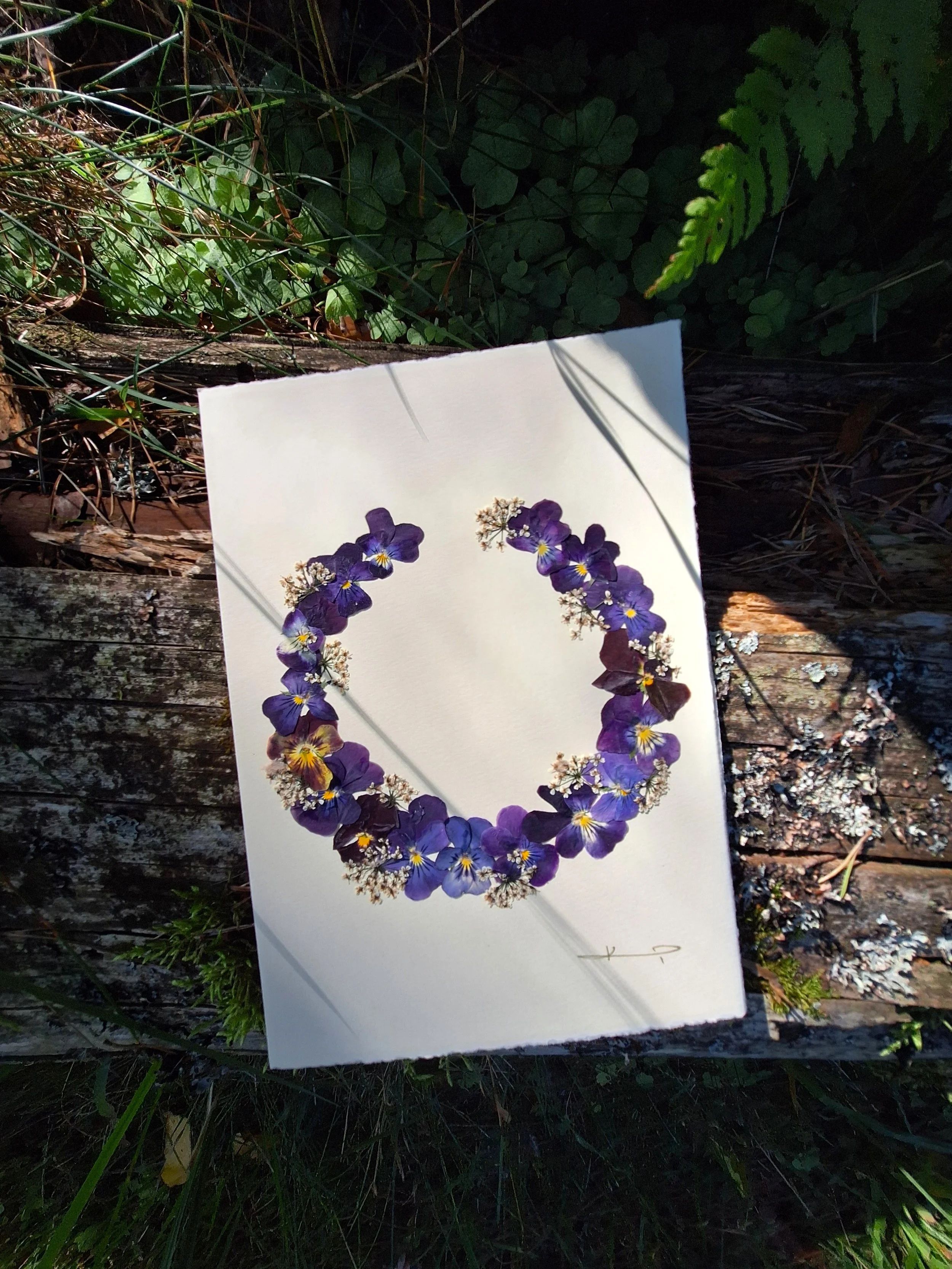 It is a unique greeting card featuring a dark purple wreath made of real pressed pansies. A gift for your loved ones or a sweet addition to your home decor.
