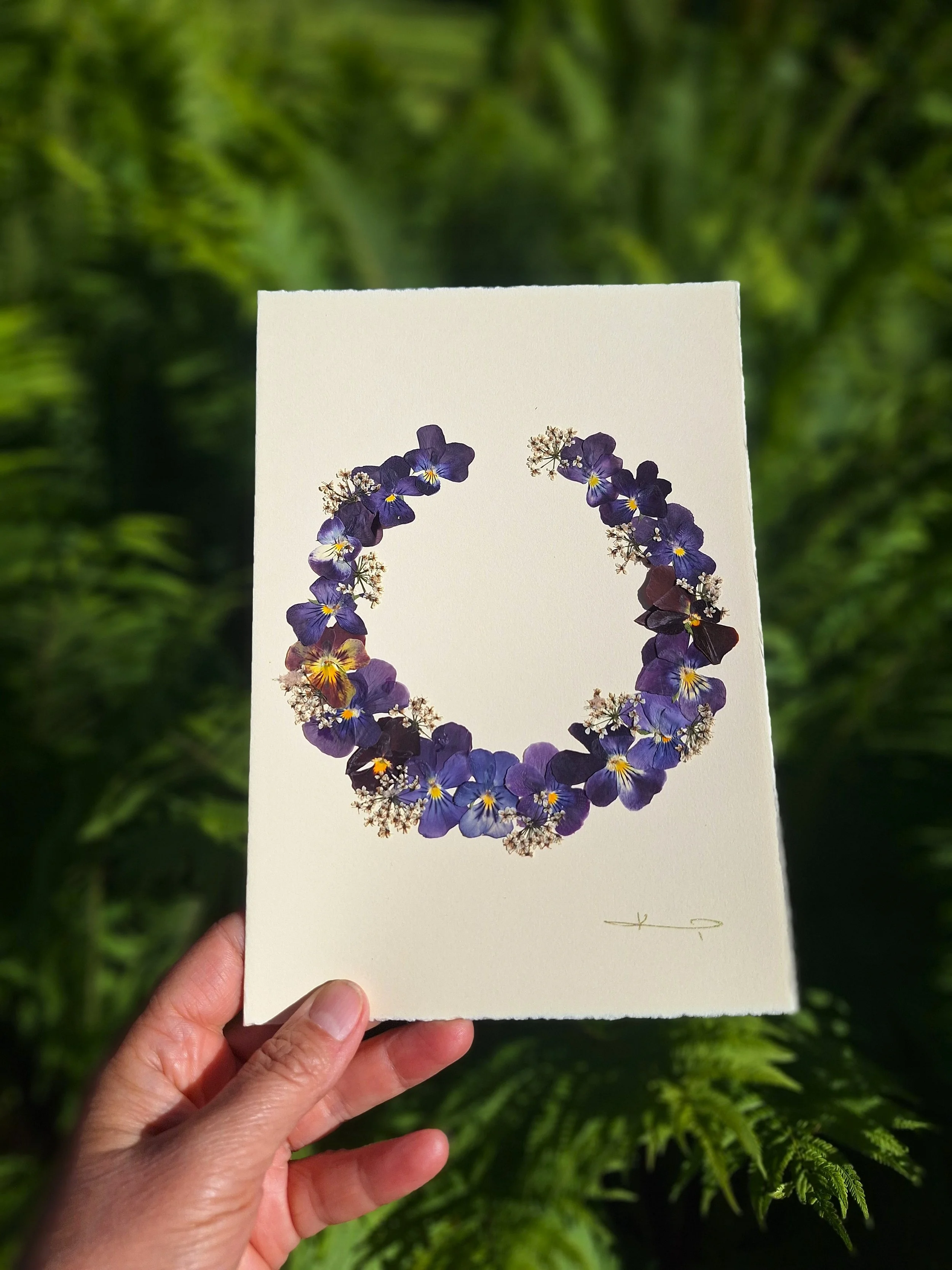 It is a unique greeting card featuring a dark purple wreath made of real pressed pansies. A gift for your loved ones or a sweet addition to your home decor.