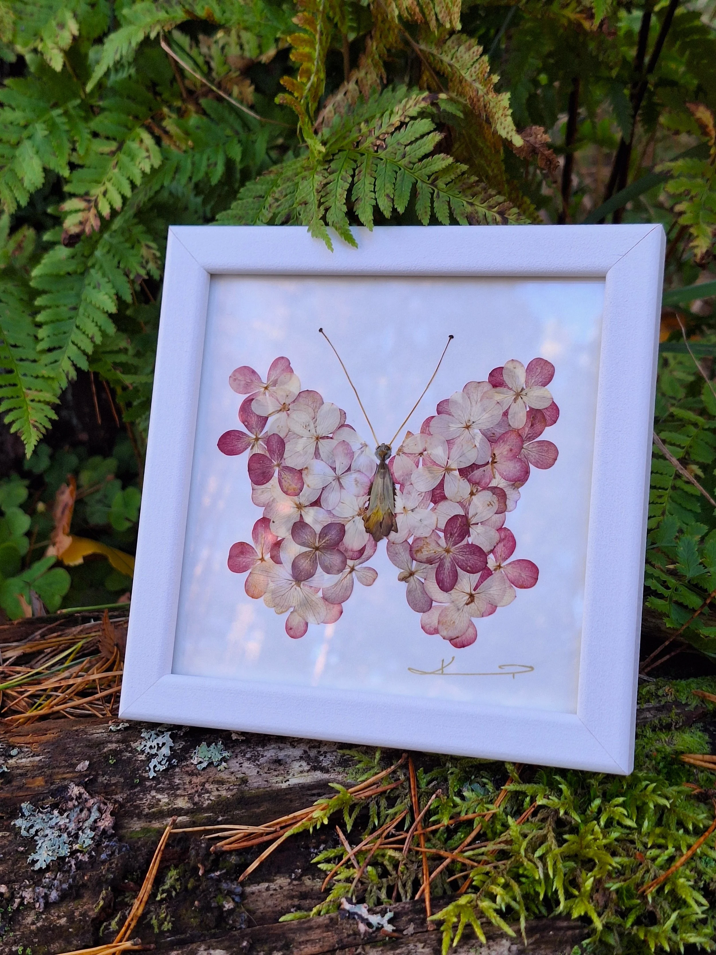 Kai Lillekaardid handmade botanical wall art showing a square white frame with a romantic butterfly mosaic made from real pressed mauve and pink hydrangea petals.