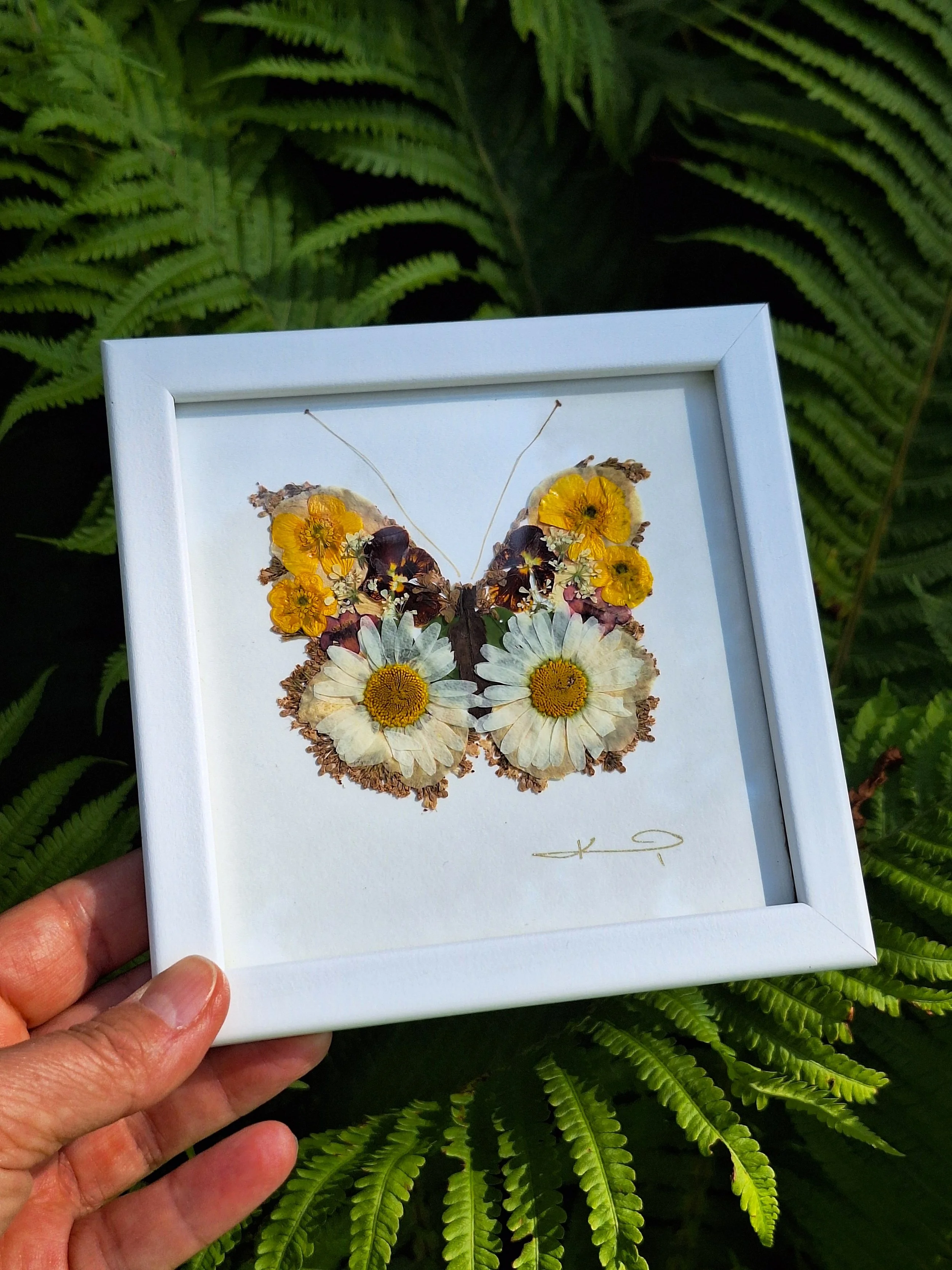 An intricate butterfly mosaic silhouette created entirely from real pressed flower petals, beautifully displayed inside a high-quality white frame.