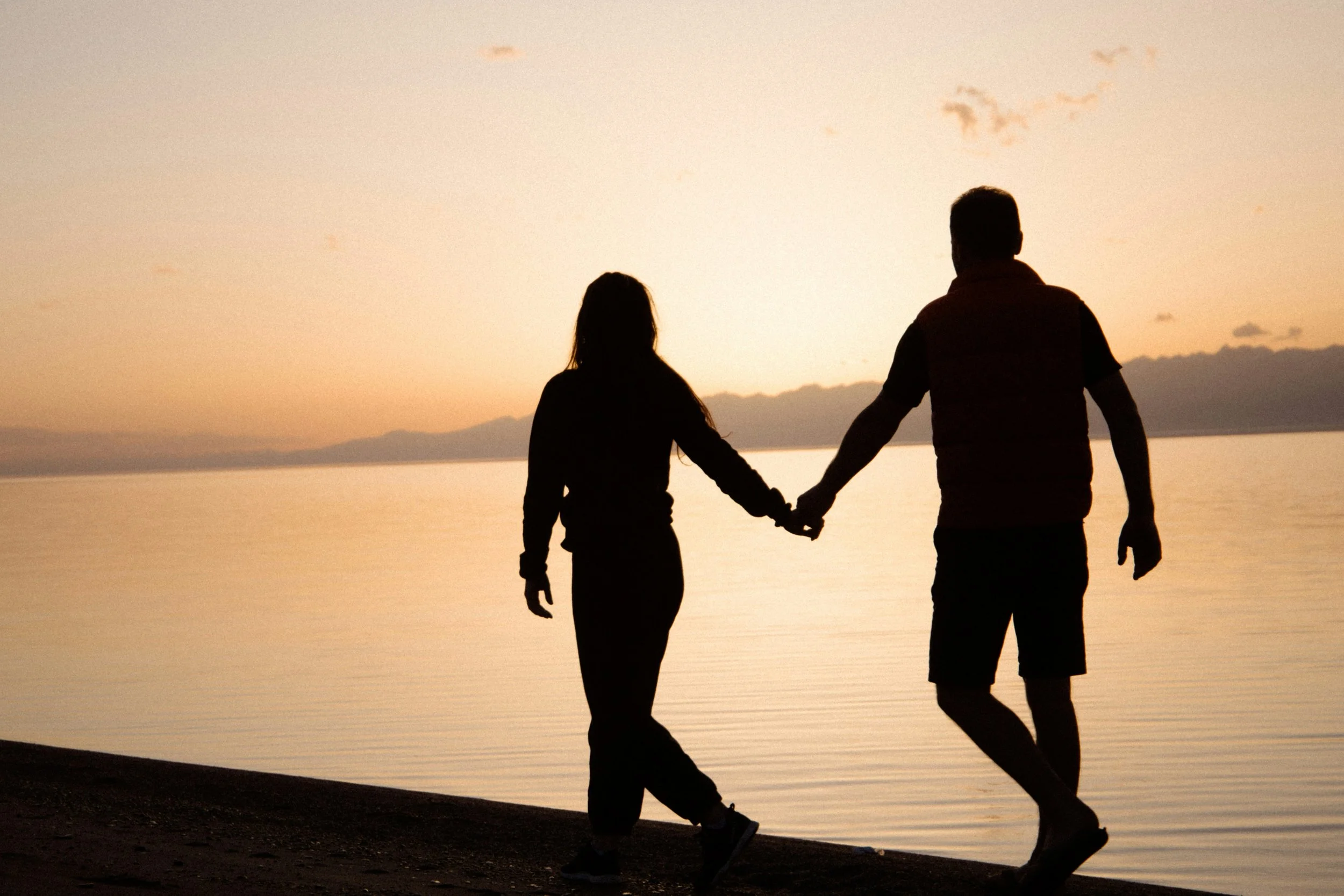 Silhouette of a couple holding hands walking along a beach during sunset.