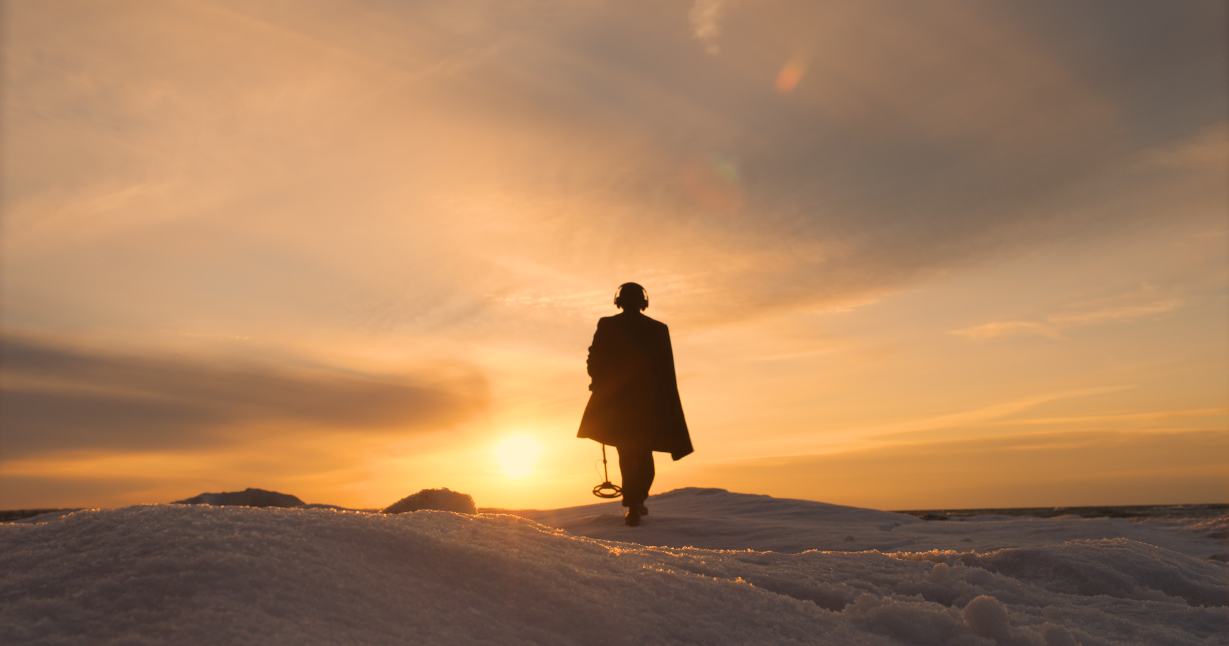 man with metal detector walking into the sunset at Chimney Bluffs State Park