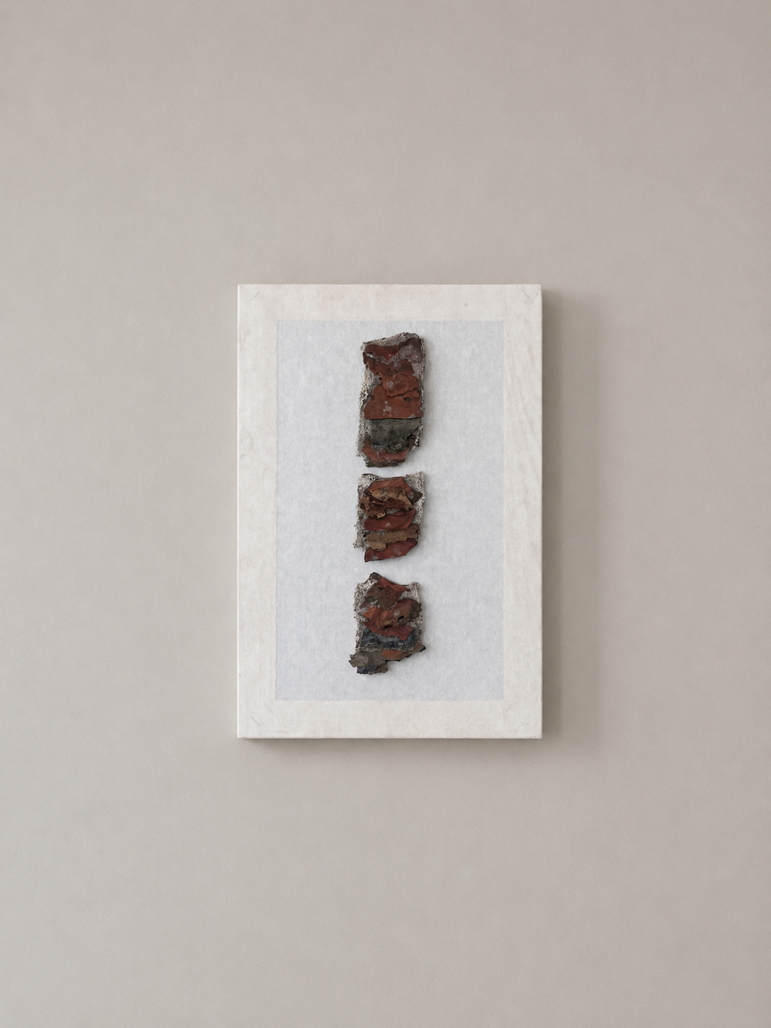 A framed artwork of three layered, irregular-shaped pieces of reddish-brown and gray textured material arranged vertically on a white background.