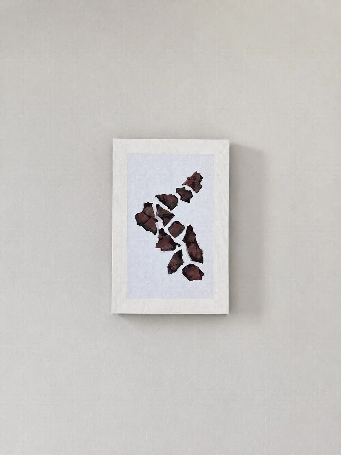 A framed artwork on a plain light-colored wall featuring an abstract pattern of dark brown irregular shapes on a white background.