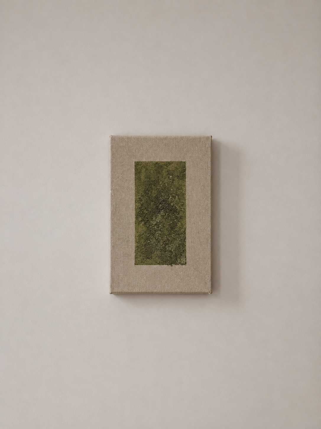 A small rectangular canvas with a textured beige border and a central abstract green pattern, mounted on a plain, off-white wall.