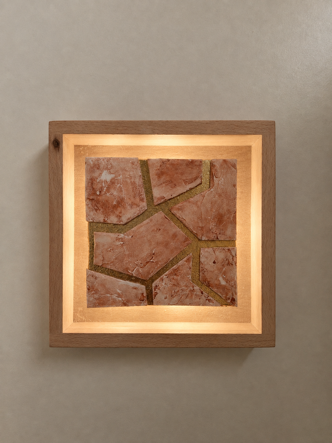 A framed mosaic artwork featuring irregularly shaped pinkish-orange stone tiles with gold-colored grout.