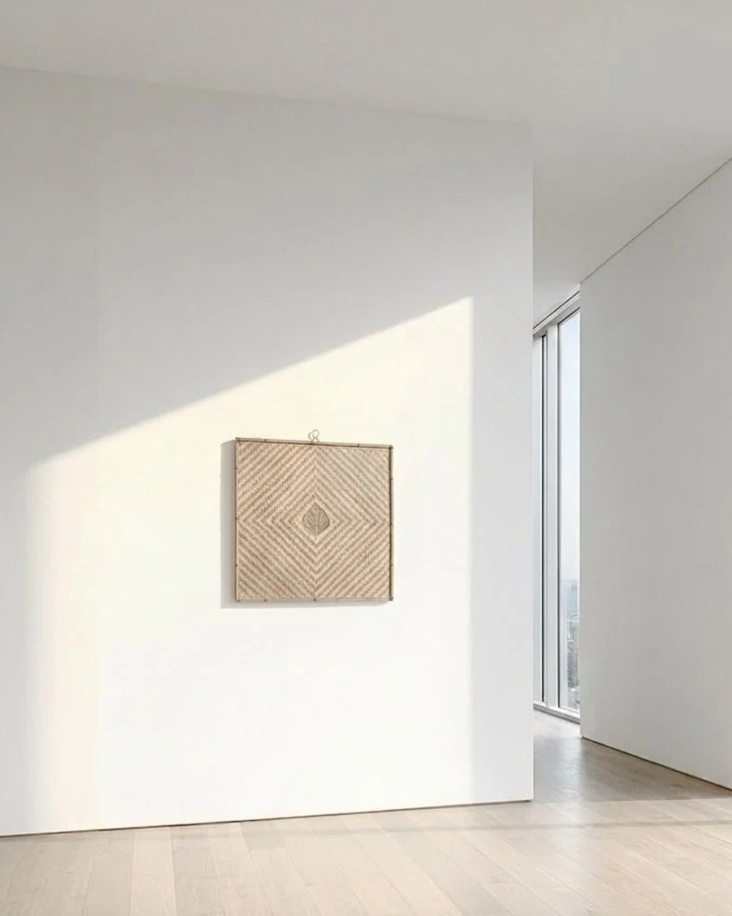 Minimalist interior with white walls and a beige woven wall hanging or artwork, sunlight casting a shadow on the wall, next to a floor-to-ceiling window.