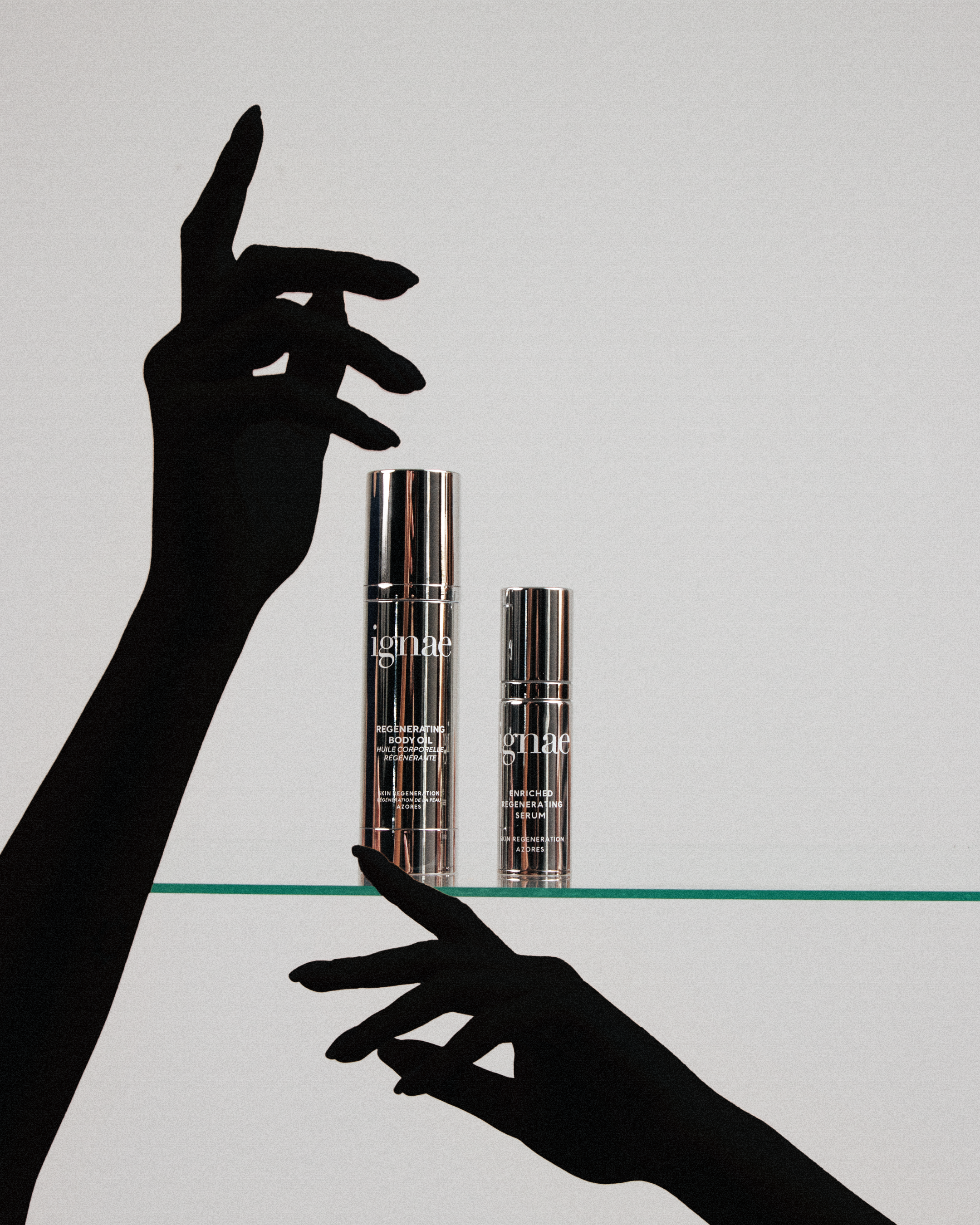 Silhouette of two hands, one reaching out and the other holding a cosmetic serum bottle, with a second smaller bottle beside it, set against a light background.