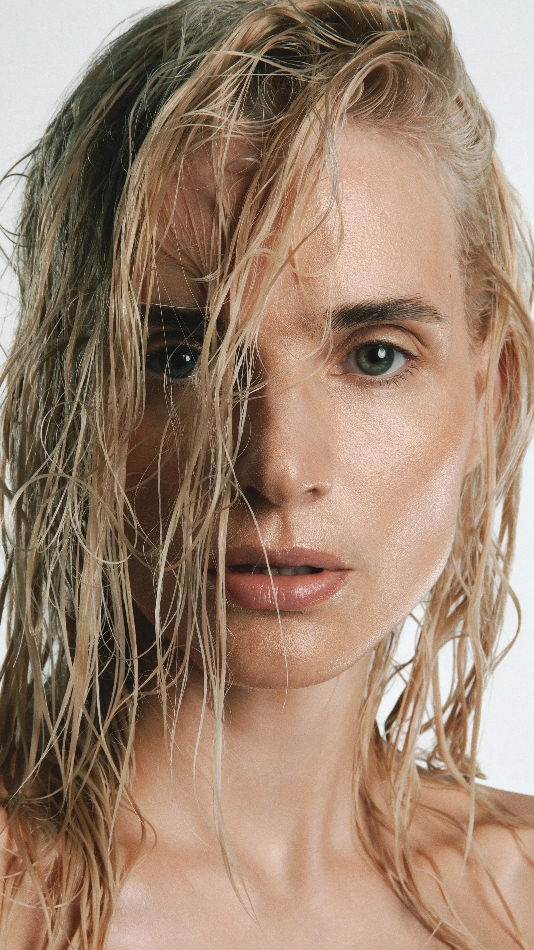 A close-up of a woman with wet blonde hair, blue eyes, and natural makeup, looking directly at the camera.
