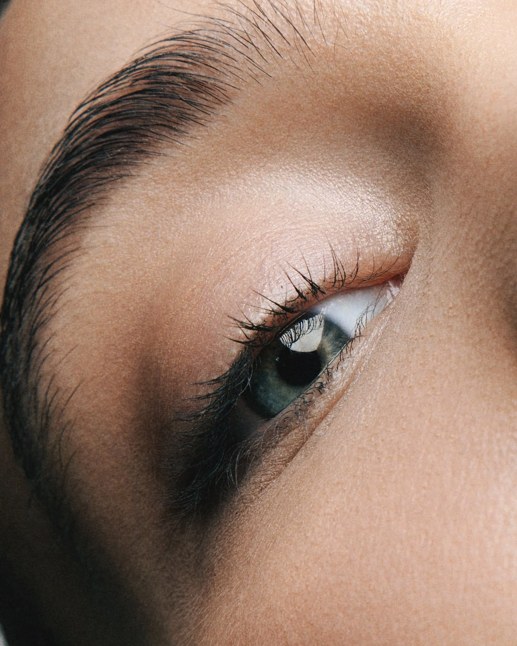 Close-up of a person's closed eye with neatly groomed eyebrows and long eyelashes.
