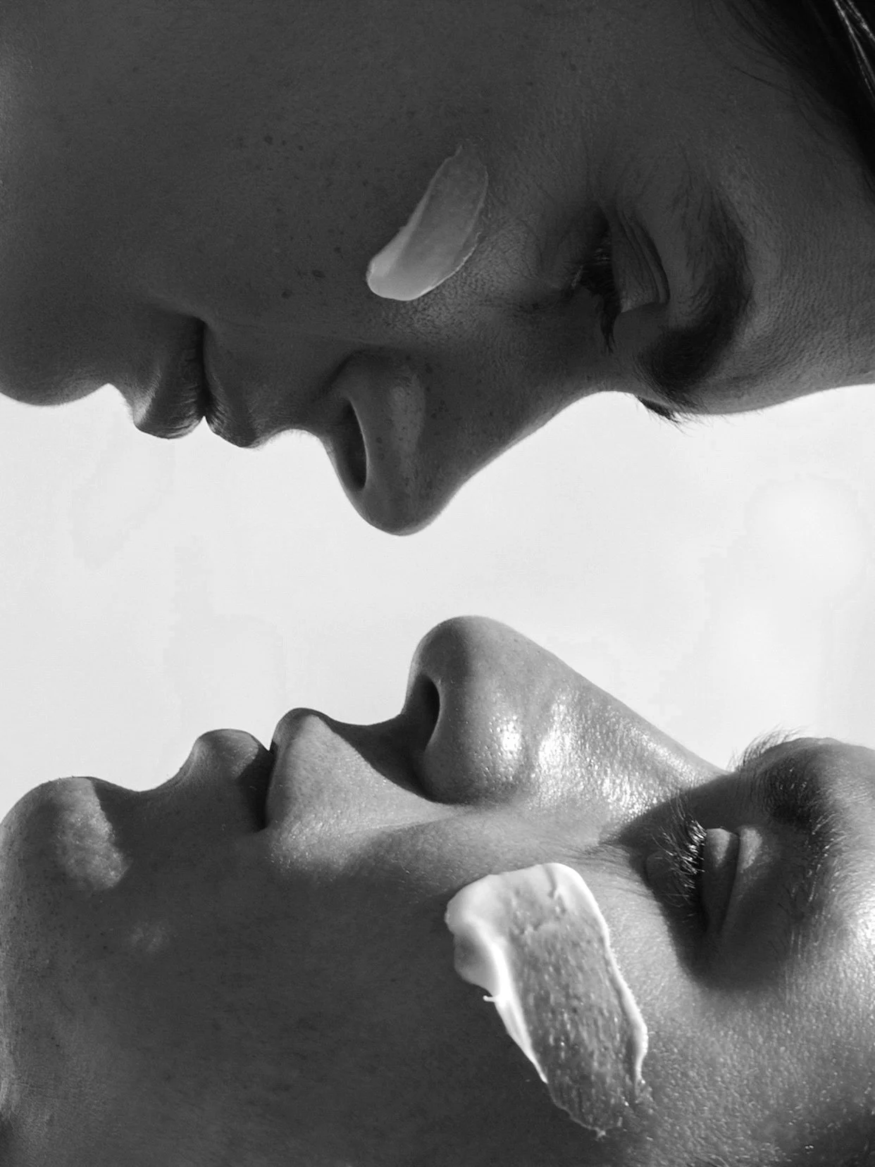 Close-up black and white photograph of a man and woman with their faces close together, both with eyes closed, with soap lather on their faces.