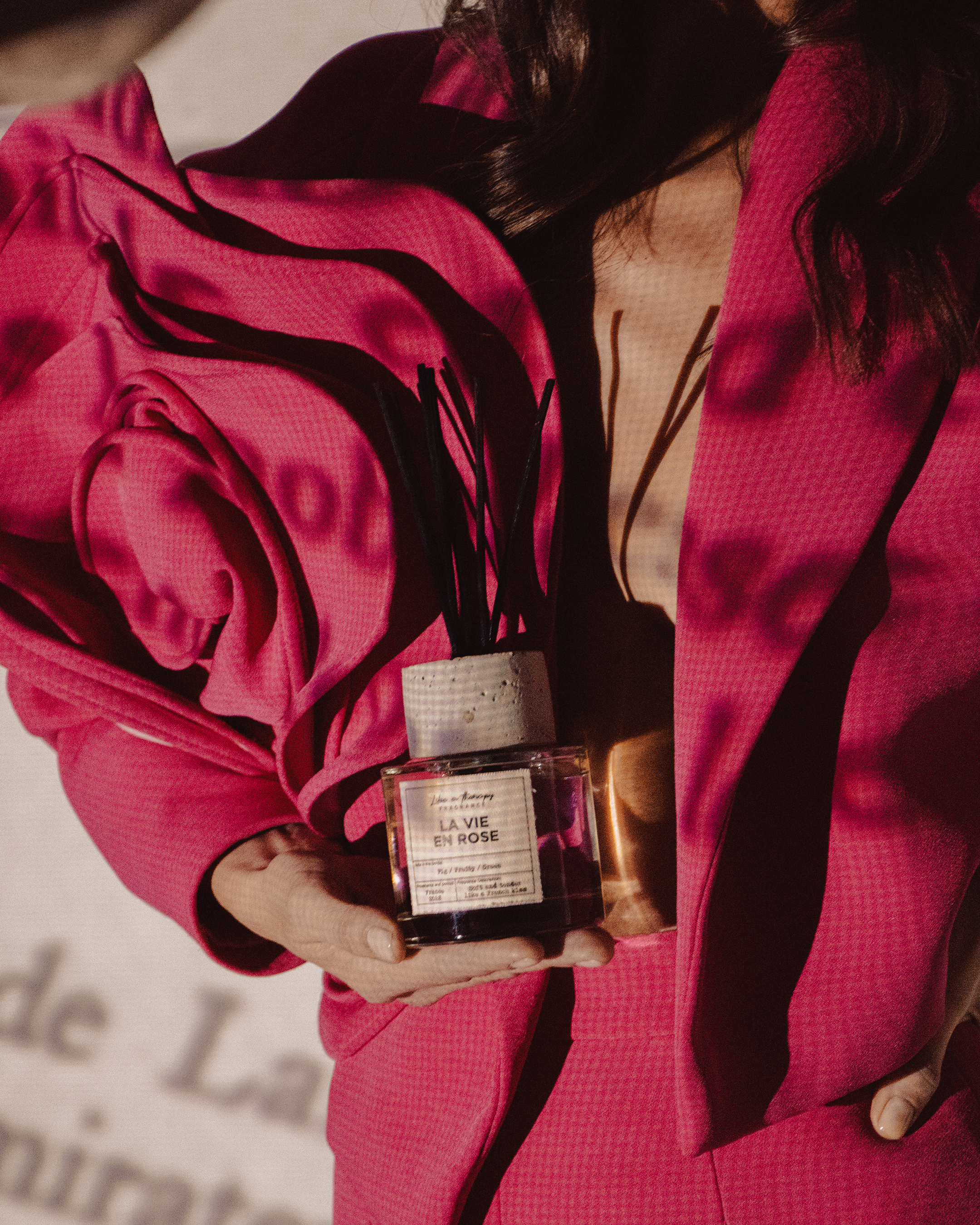 Person in a pink checkered blazer holding a small perfume bottle labeled "La Vie En Rose".