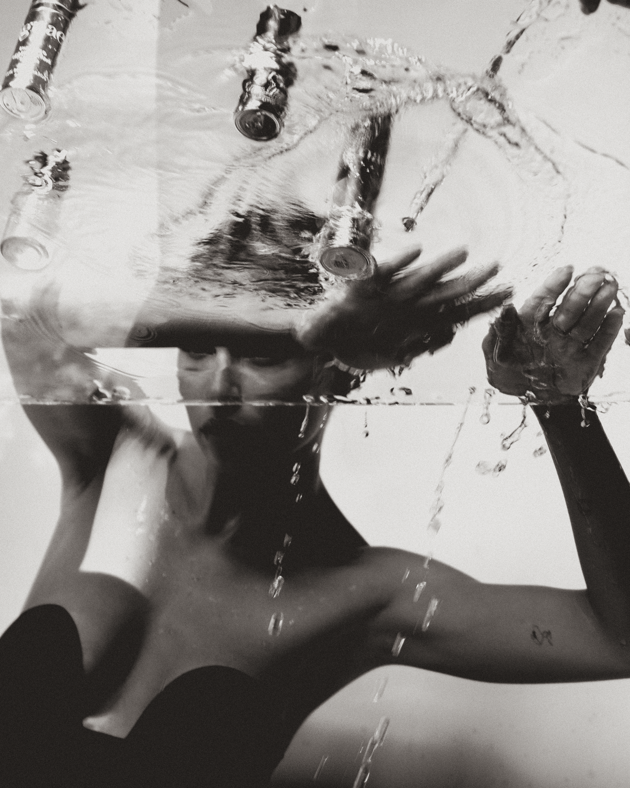 A person in dark clothing is washing their legs with water splashing around. The photo is in black and white.