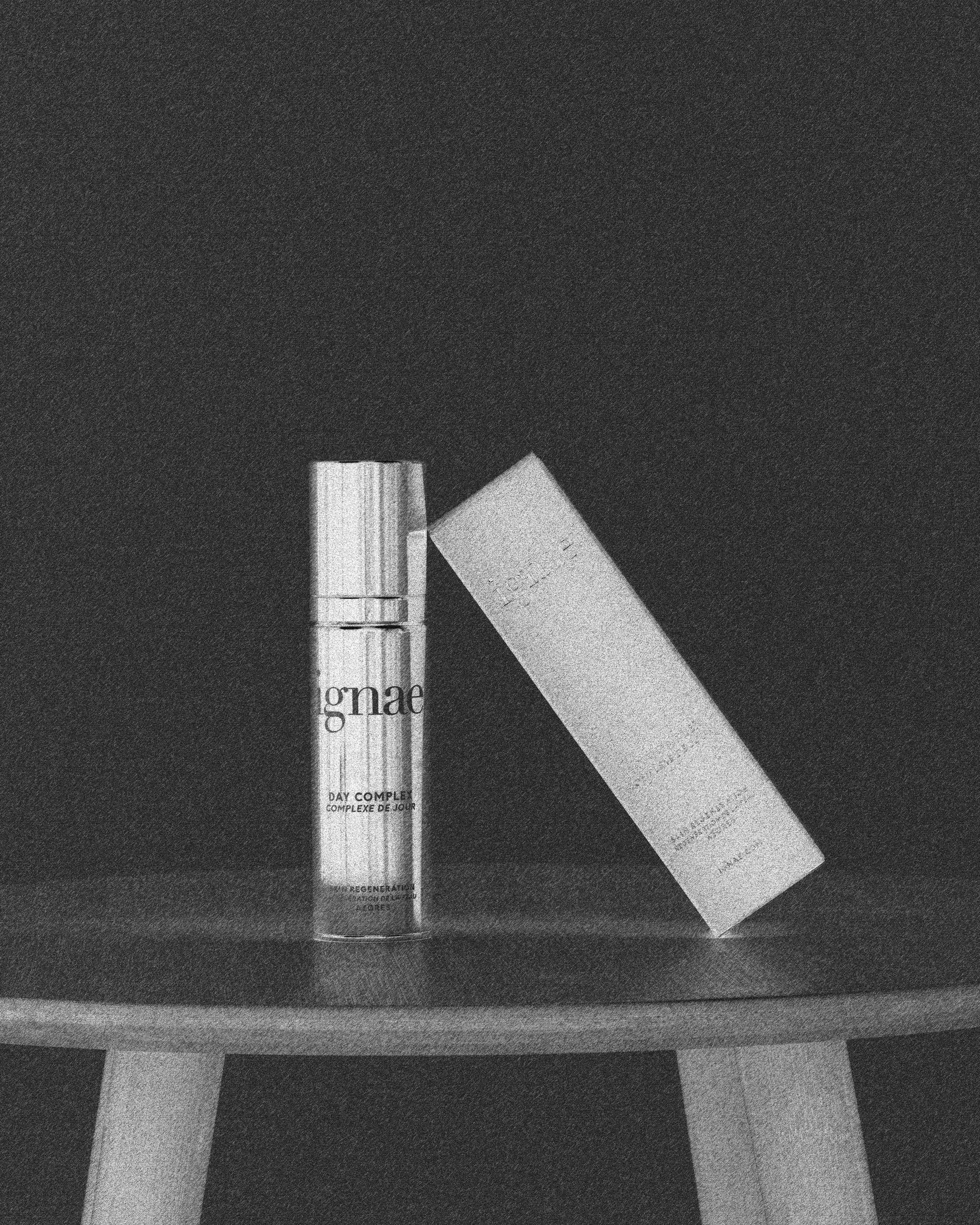 Two skincare product containers, one larger box and one smaller bottle, placed on a dark surface.