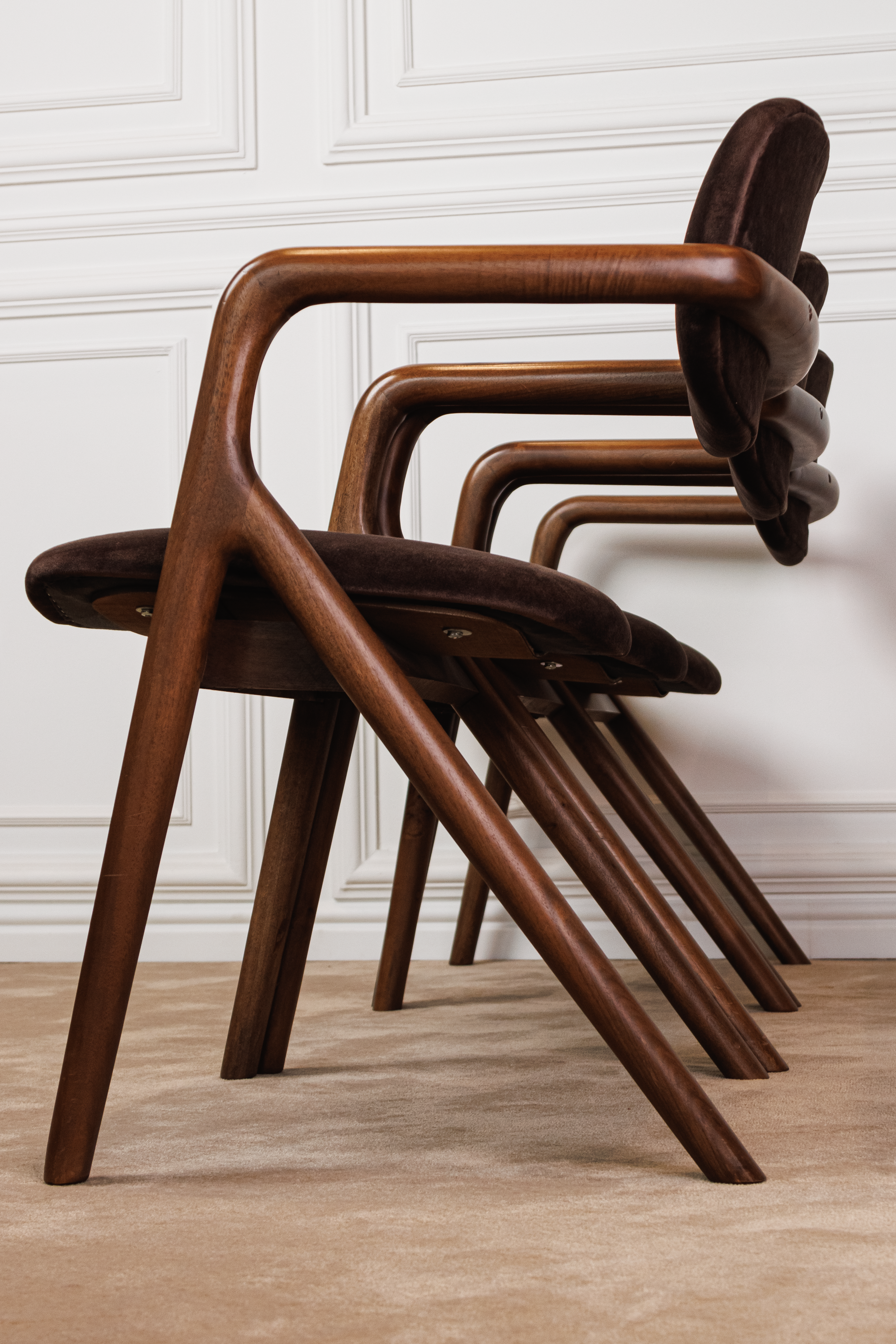 A row of four wooden chairs with curved armrests and dark upholstered seats, placed on a beige carpet in front of white paneled walls.