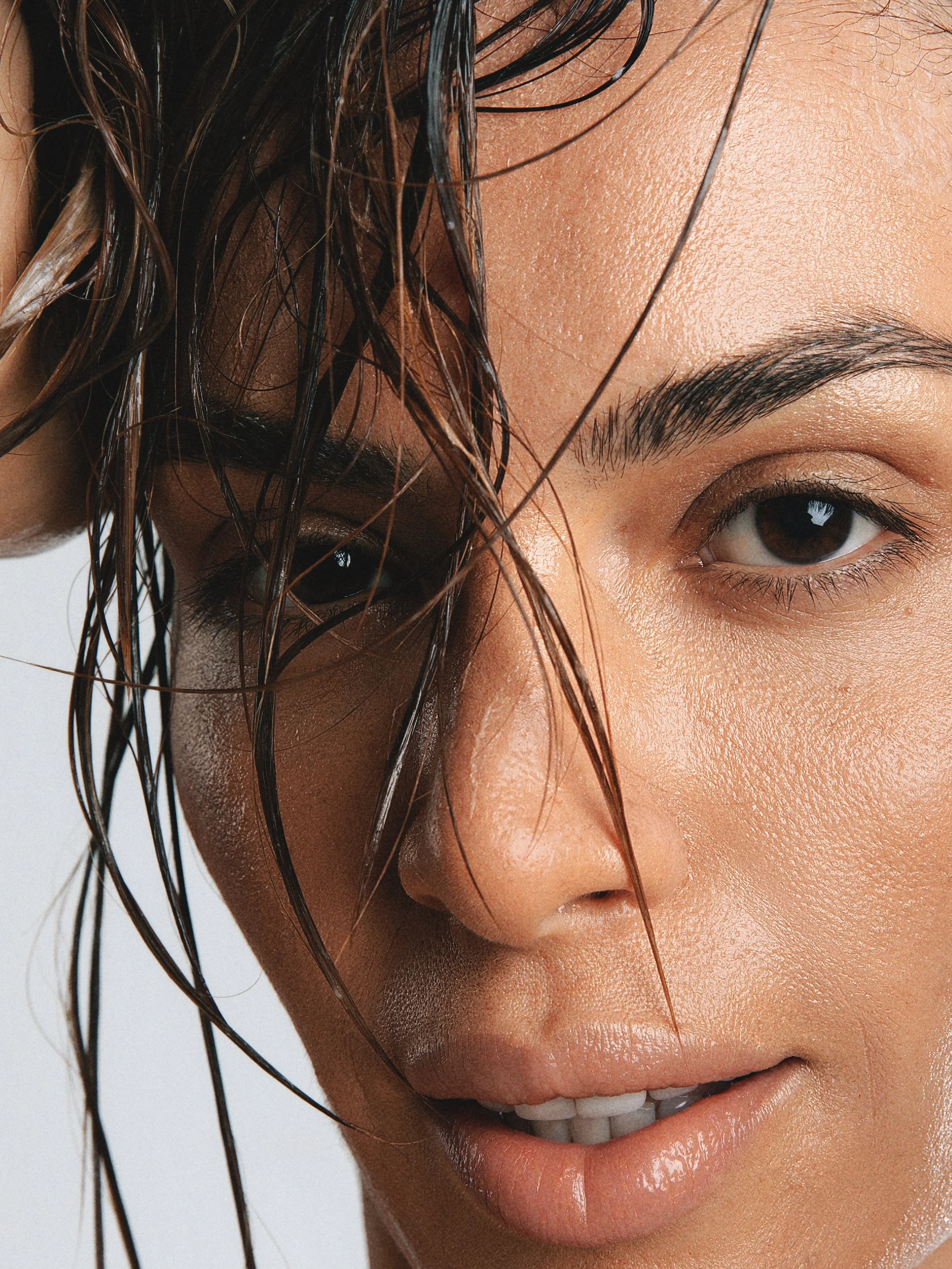 Close-up of a smiling woman's face, showing wet hair, eyebrow, eye, and lips with a white background.