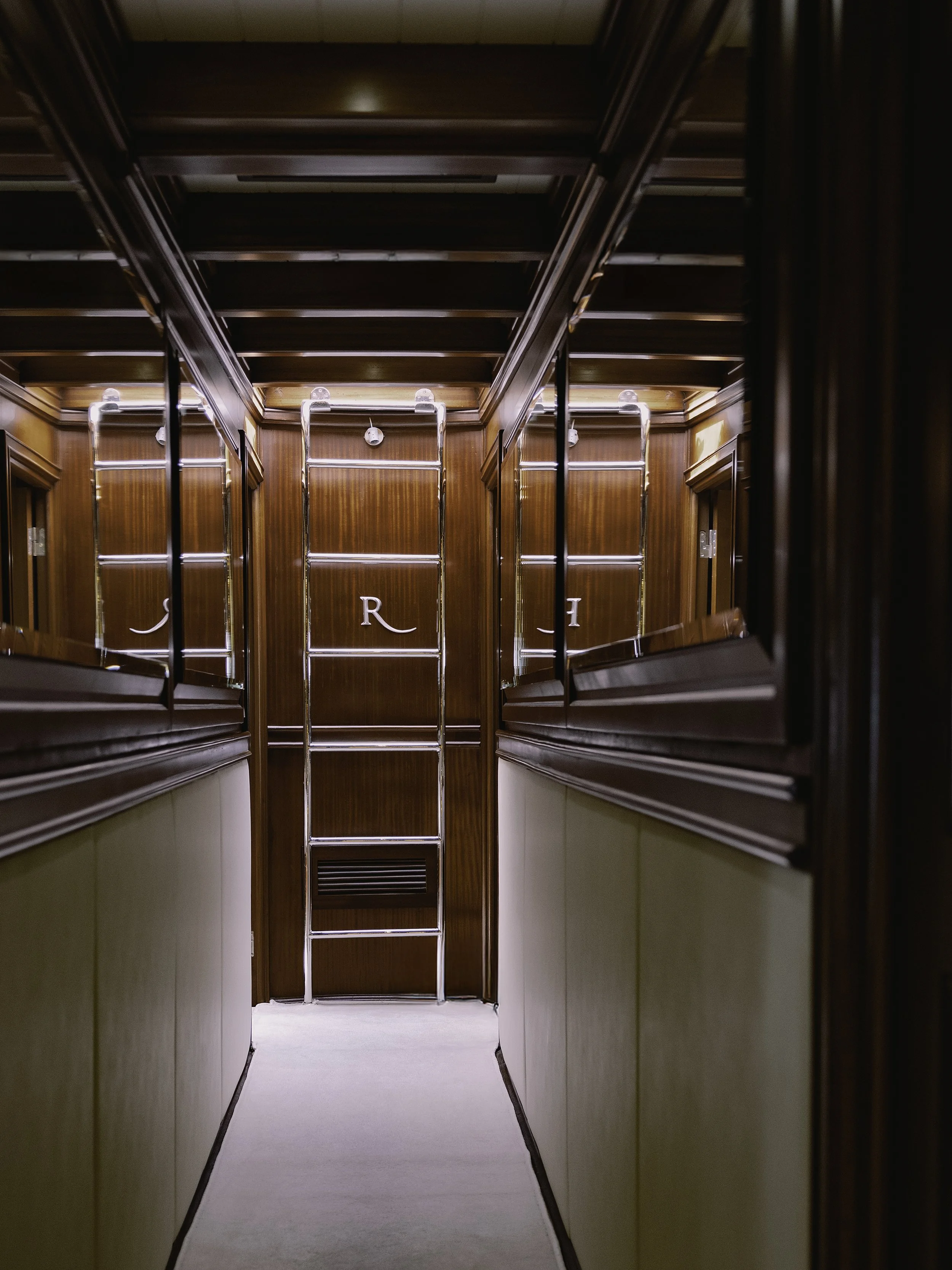 View of an elevator interior with wood-paneled walls, a metal ladder leading to the ceiling, and partially visible letters 'J R I' on the back wall.